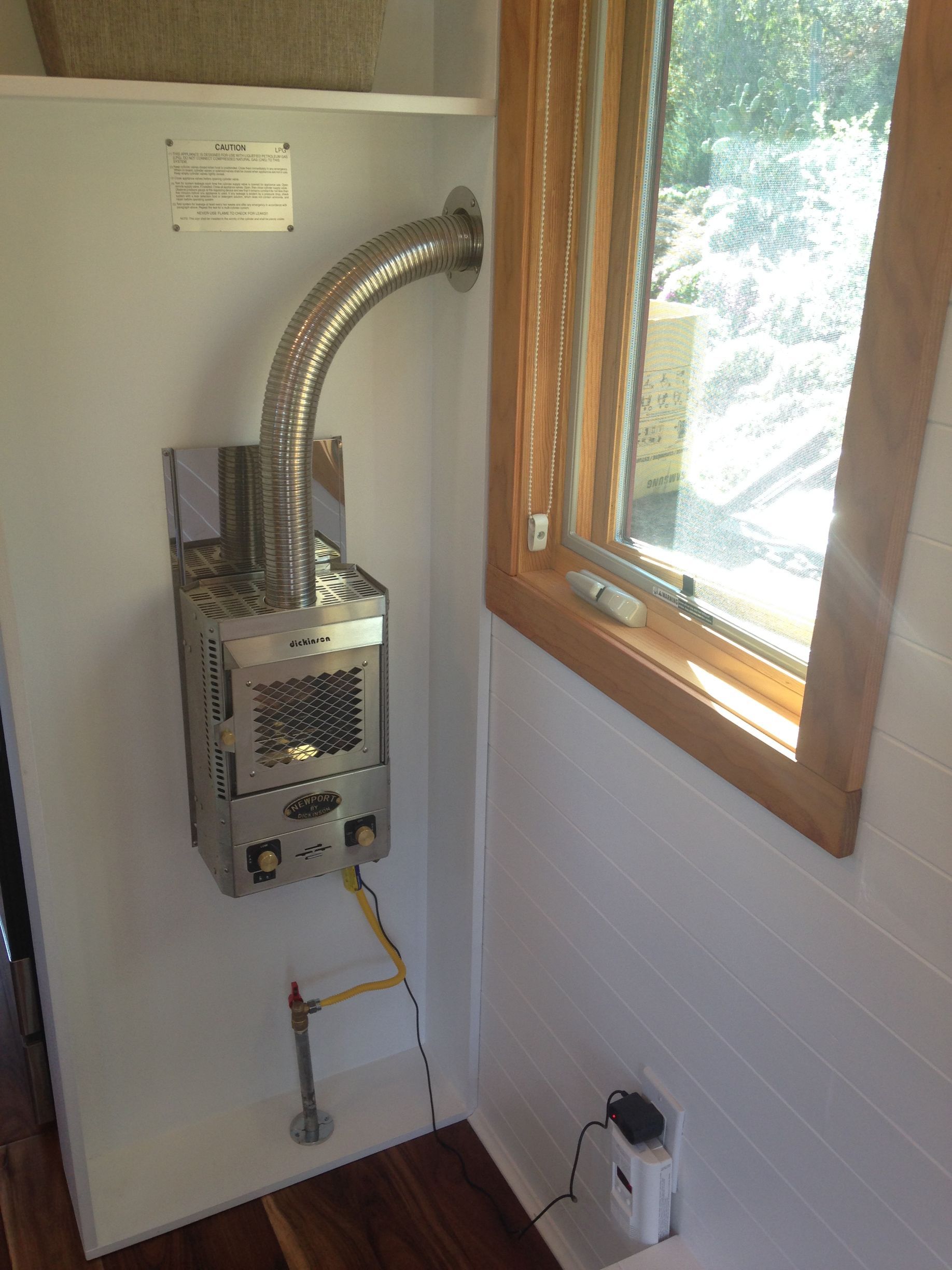 Water heater installed inside a small white room with a window and wood trim.