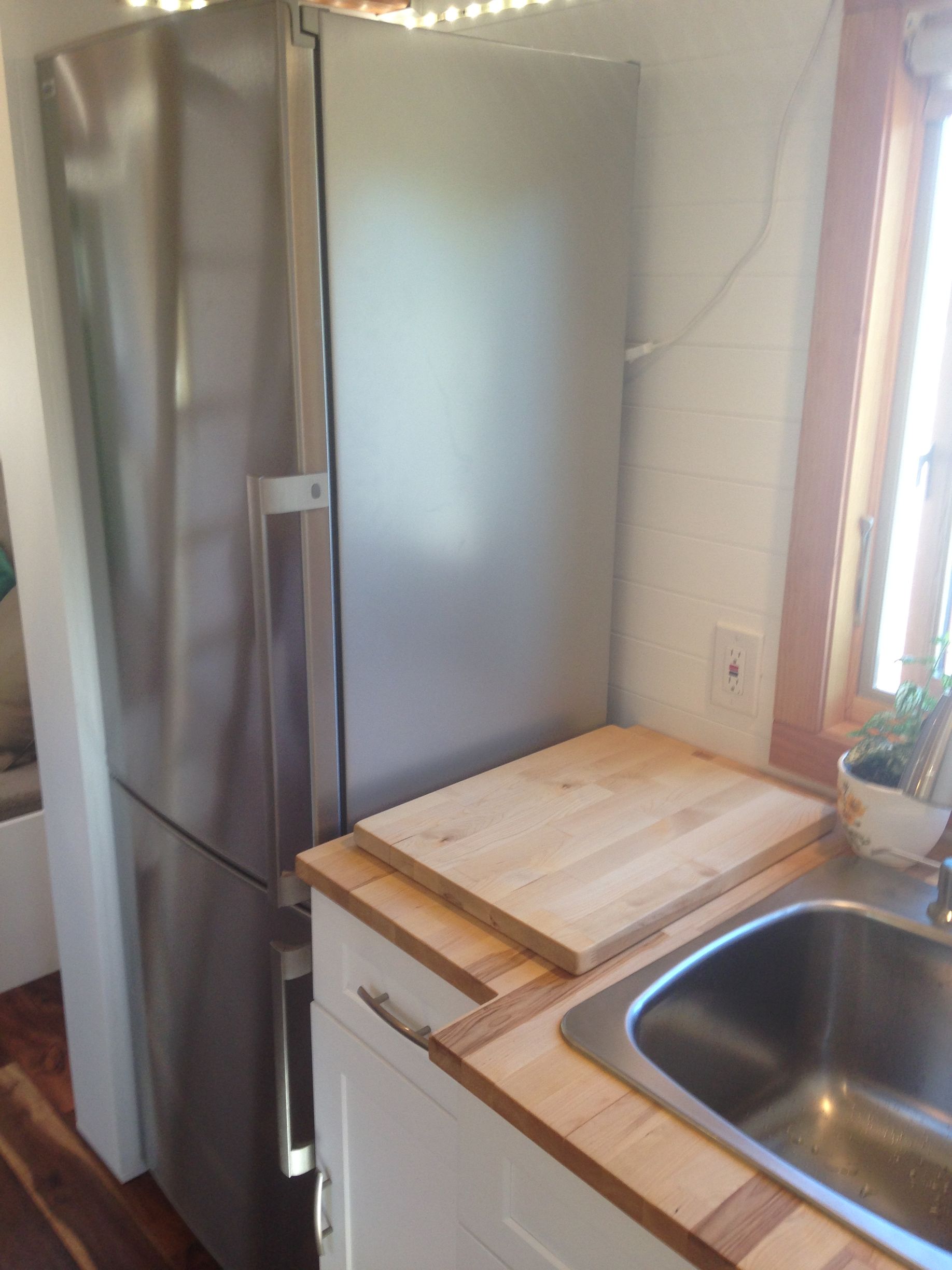 Stainless steel refrigerator next to a white cabinet and a stainless steel sink. Wooden countertops and a window.