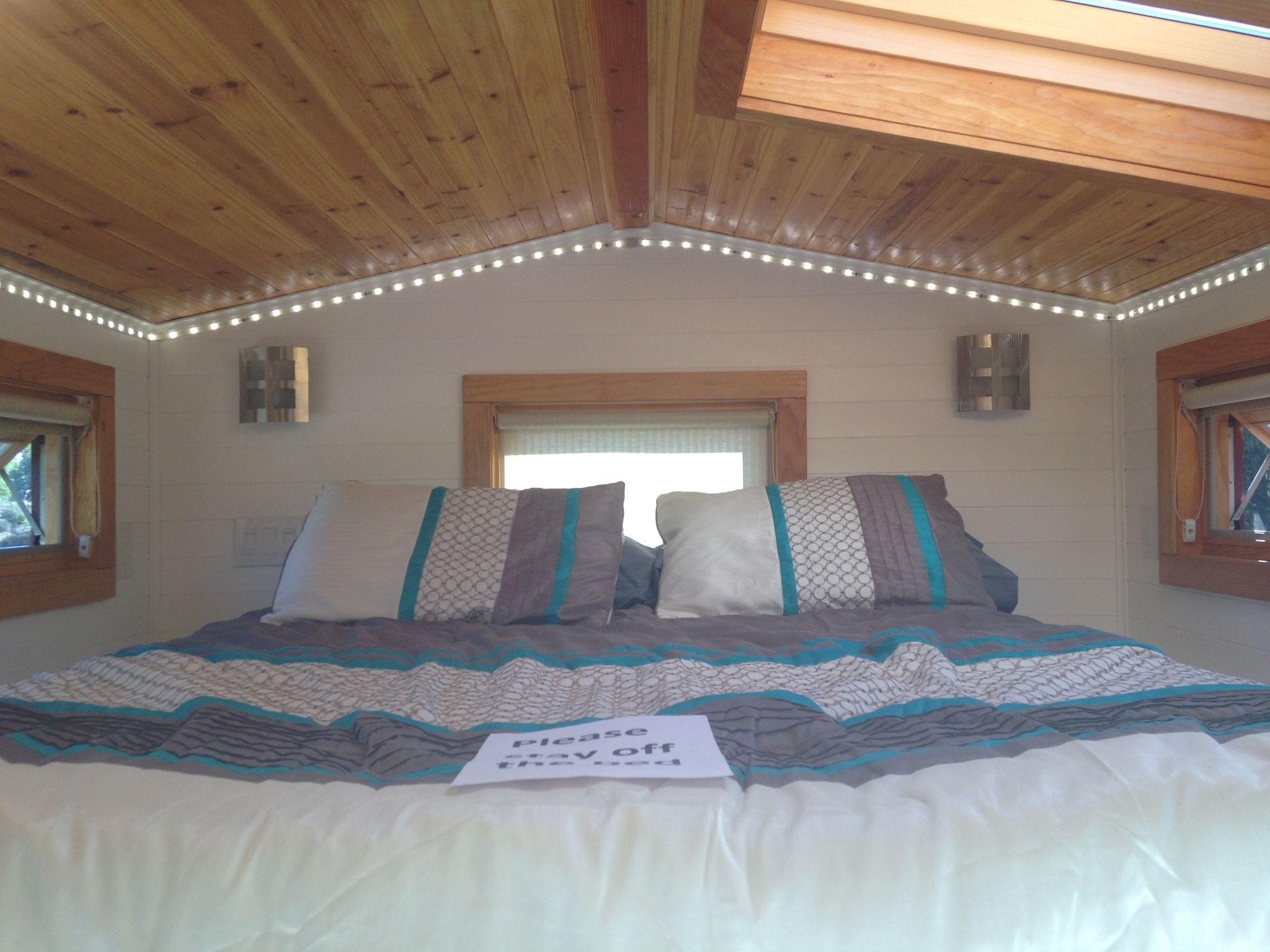 Bedroom with king-sized bed, wood ceiling, teal and gray bedding, built-in lighting, and small windows.