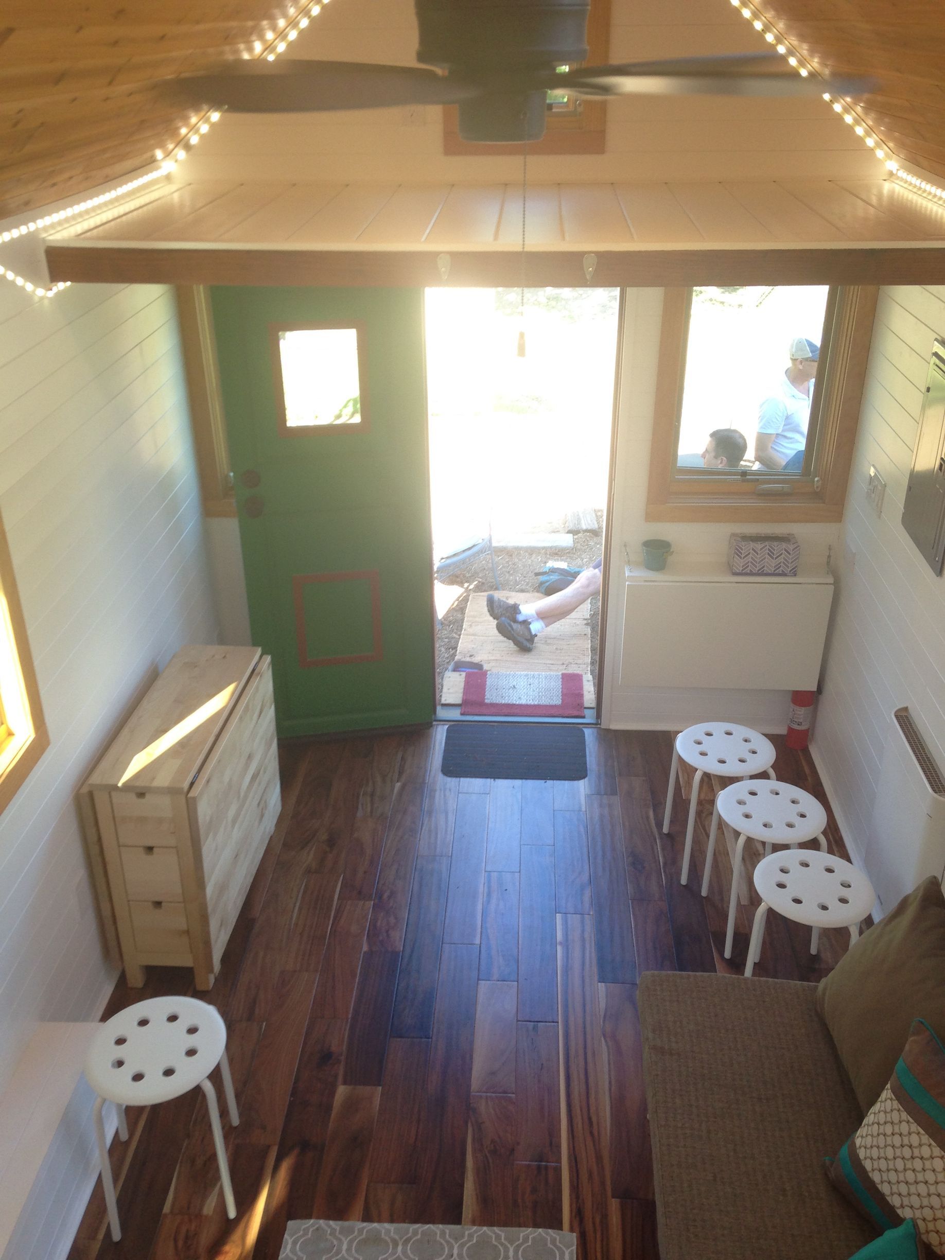 Interior of tiny house with wooden floor, green door, open doorway, stools.