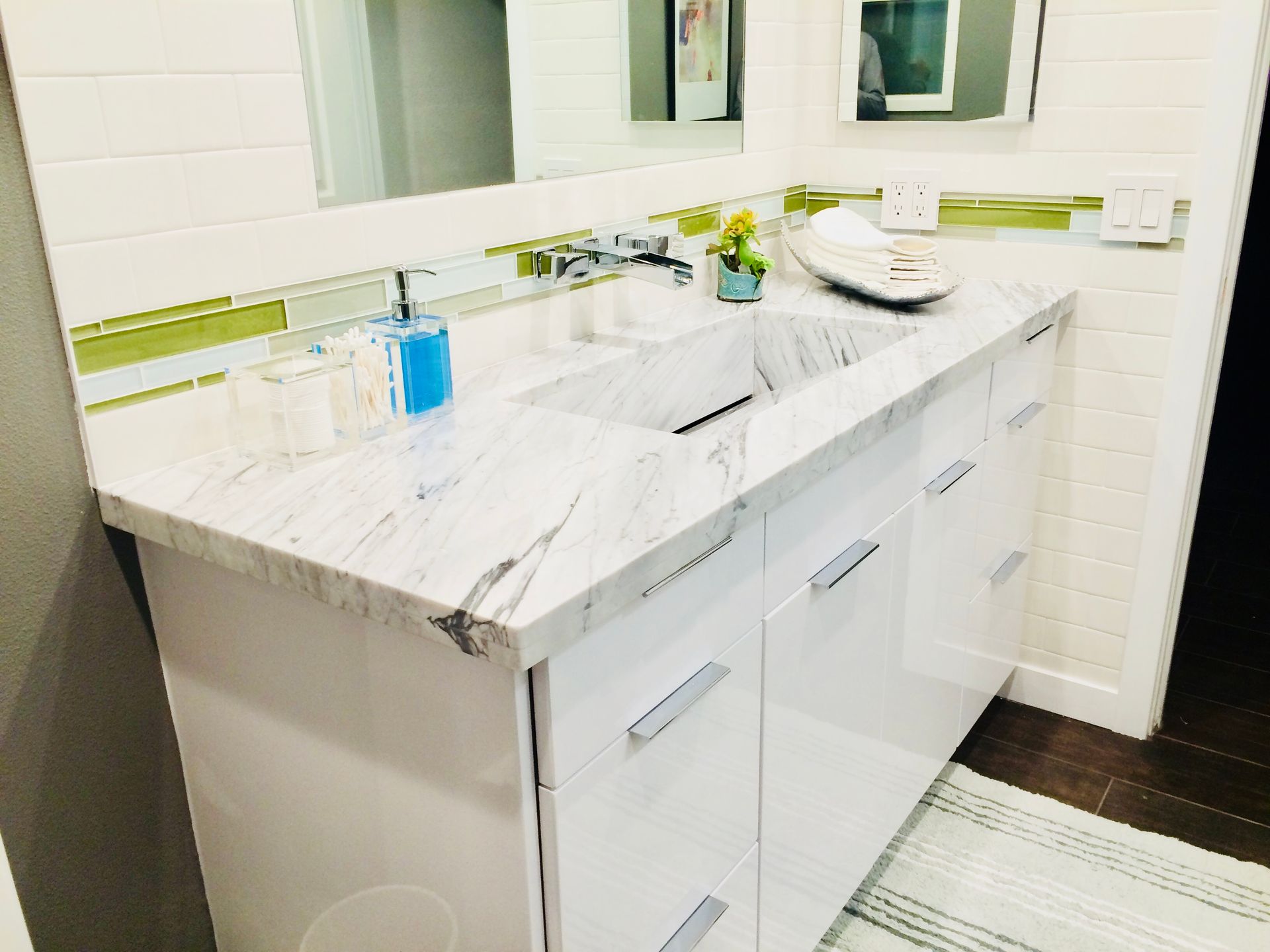 White bathroom vanity with marble countertop, chrome faucet, and green tile backsplash.