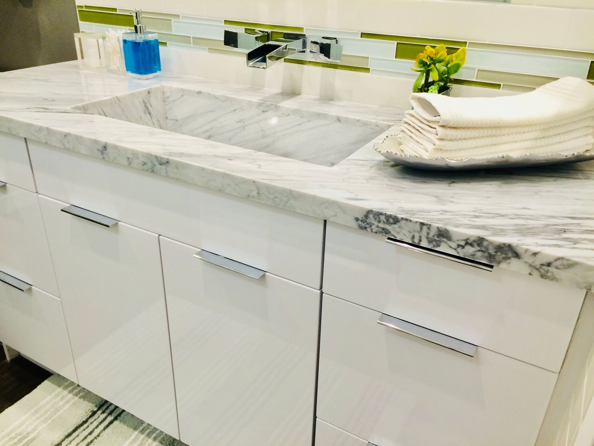 White bathroom vanity with marble countertop and sink, chrome faucet, and stacked white towels.