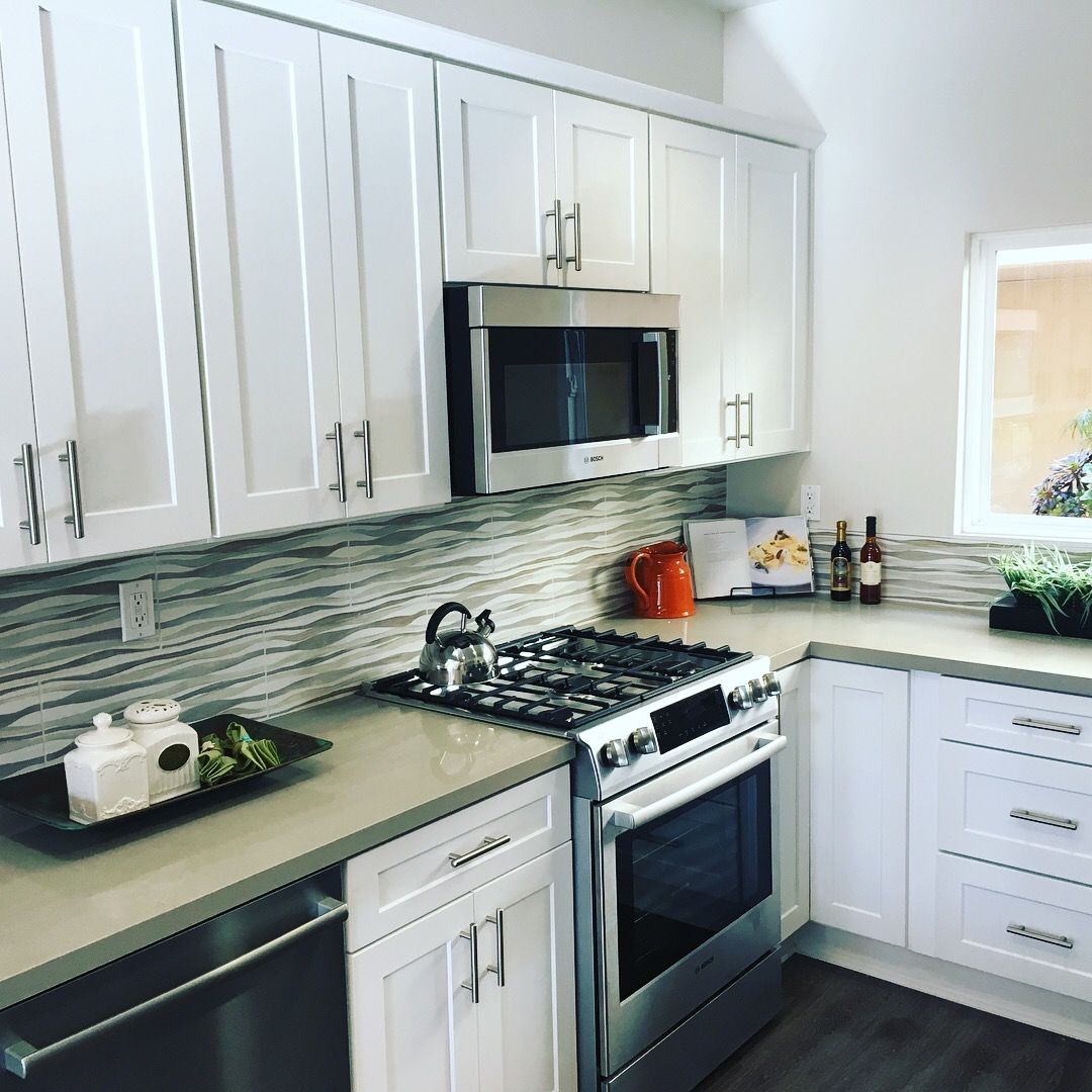 White kitchen with stainless steel appliances, white cabinets, and grey countertops.