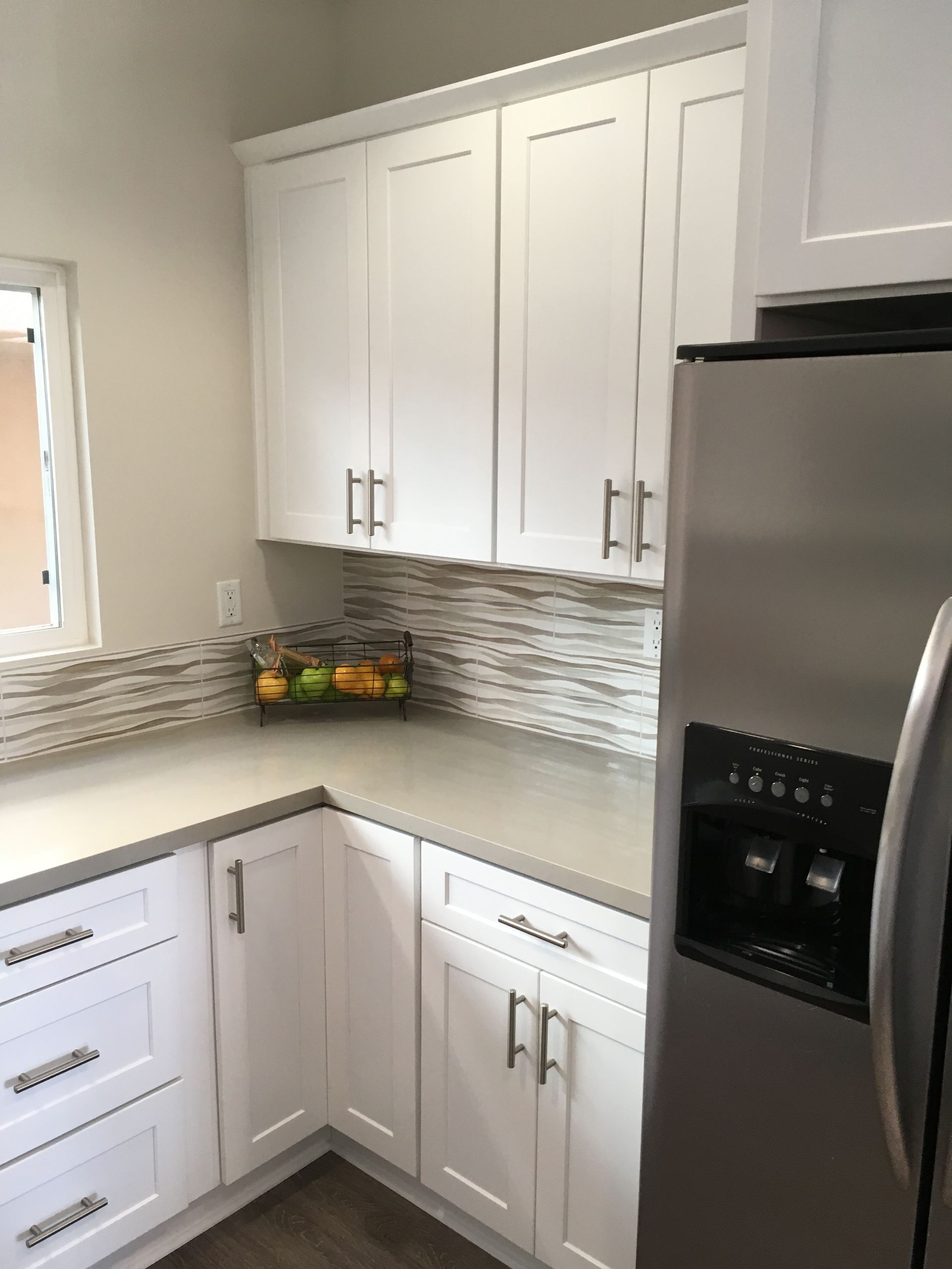 White kitchen with cabinets, stainless steel refrigerator, and light countertop.