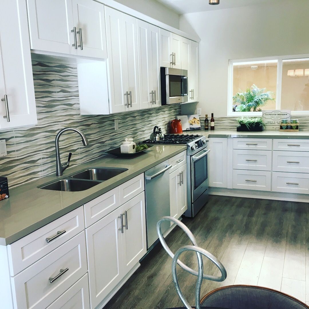 White kitchen with gray countertops, stainless steel appliances, and wood-look flooring.