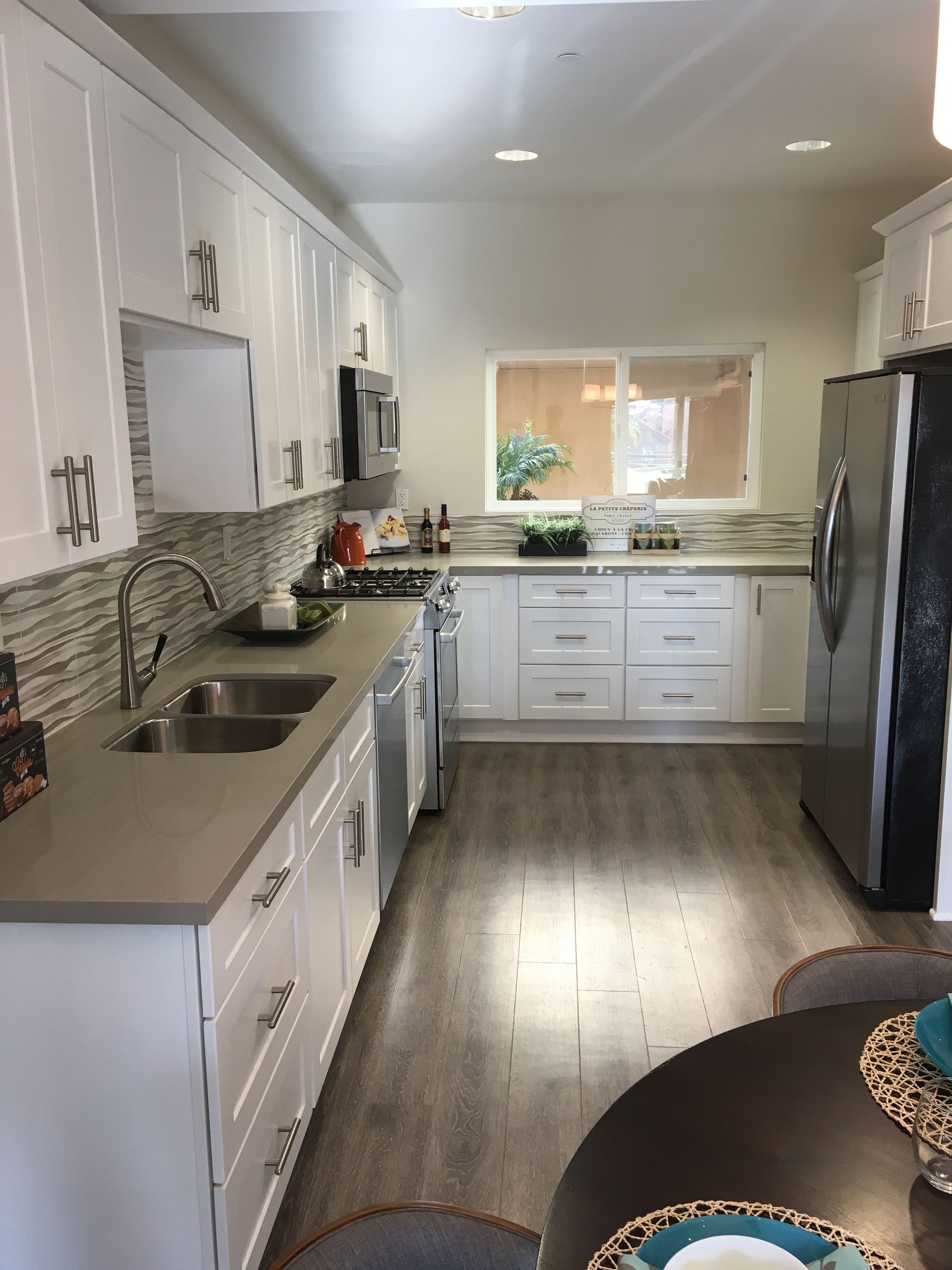 White kitchen with gray countertops, stainless steel appliances, and a window.