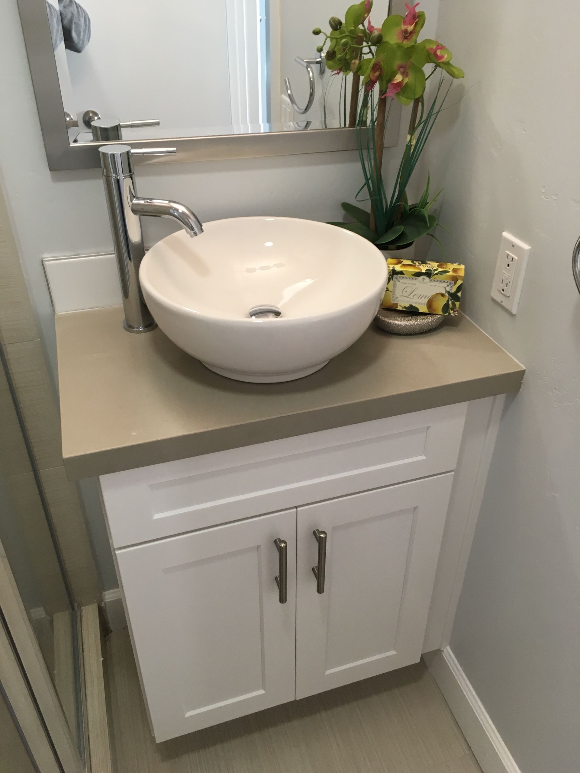White vanity with a bowl sink and chrome faucet. The countertop is light gray.