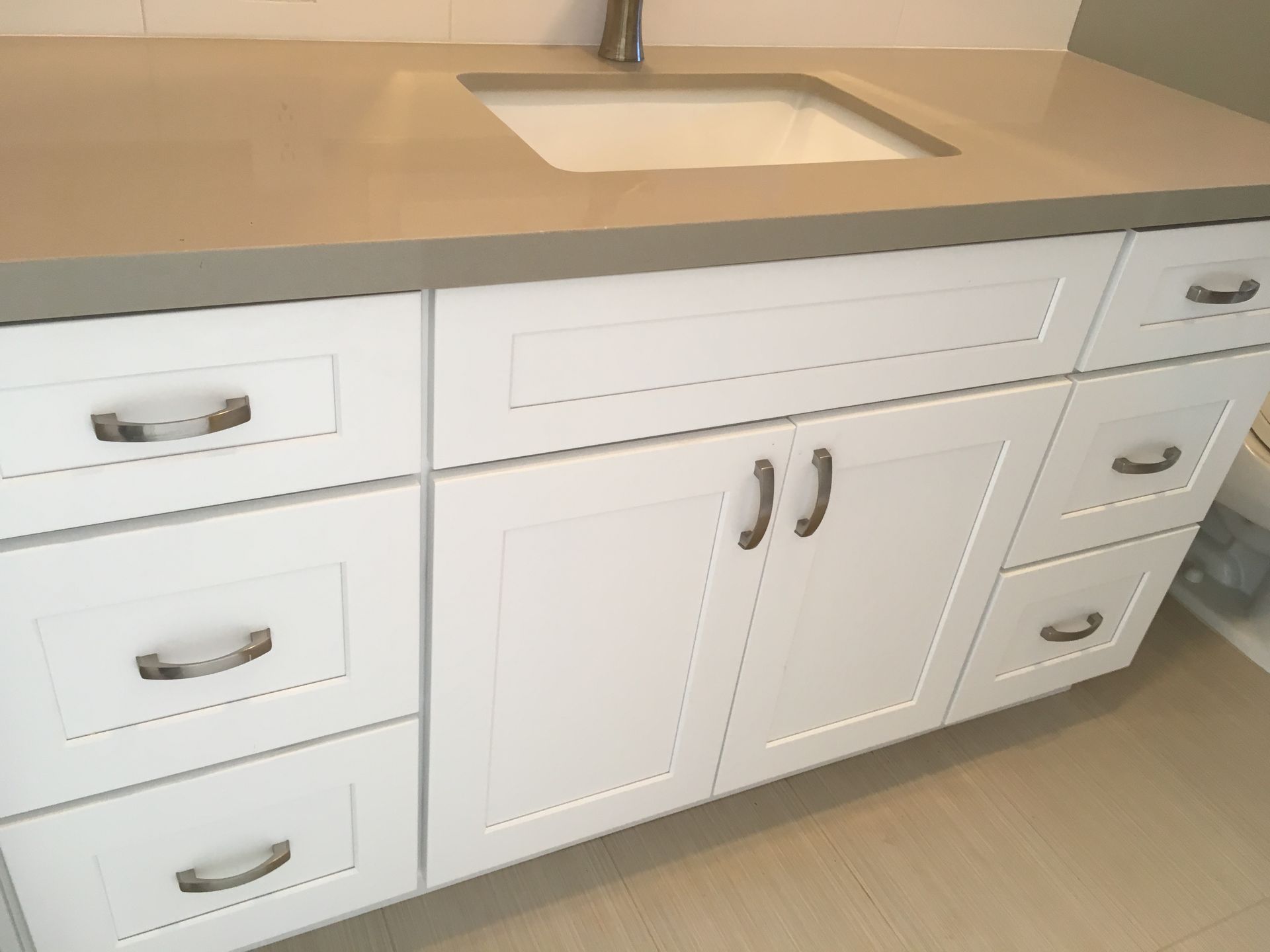 White bathroom vanity with drawers and doors, grey countertop, silver hardware.