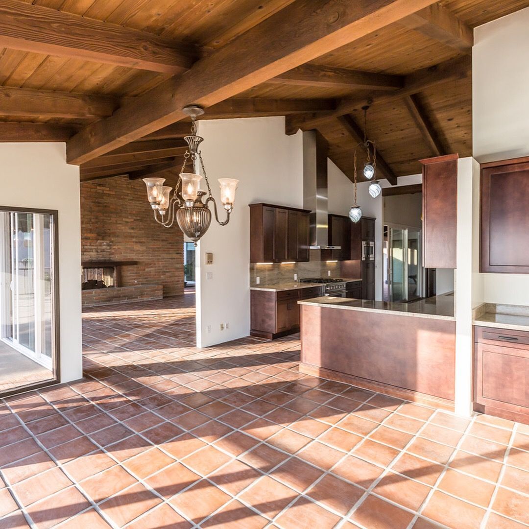 Spacious interior with terracotta tile floors, wooden beams, kitchen with dark cabinets, and a chandelier.