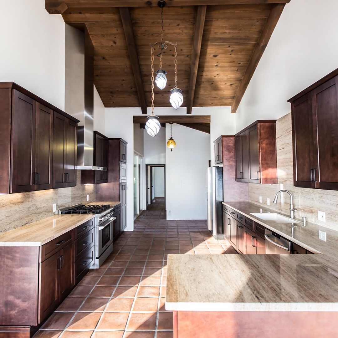 Kitchen with brown cabinets, wood ceiling, tile floor, stainless steel appliances, and granite countertops.