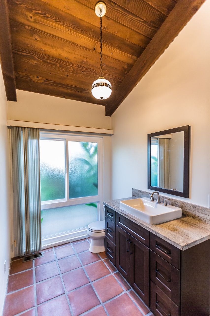 Bathroom with dark wood vanity, stone countertop, terracotta tile floor, and window.