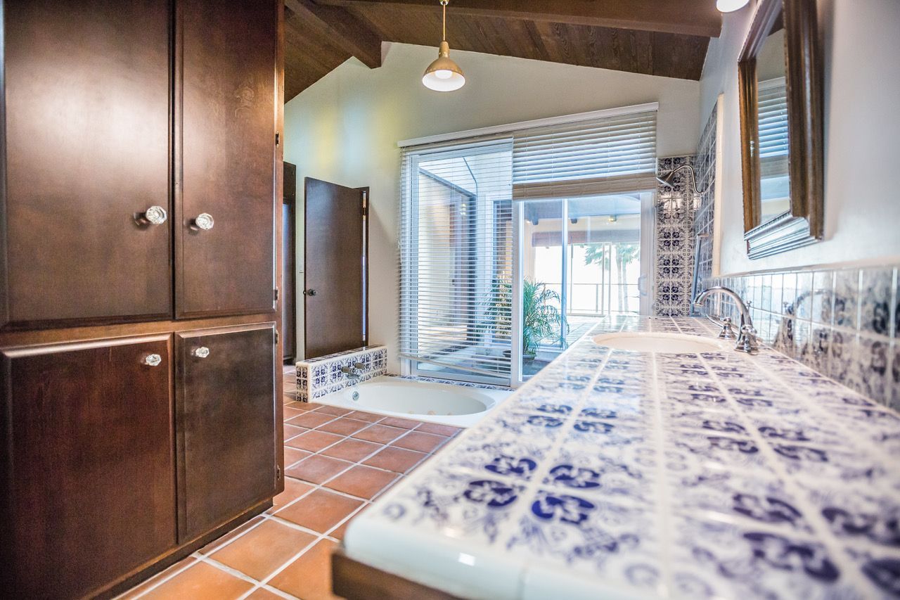 Bathroom with dark cabinetry, blue and white tile counter, and a shower with a view to the outside.