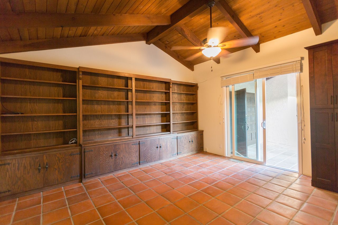 Empty room with built-in wooden bookshelves, terracotta tile floor, and sliding glass door.