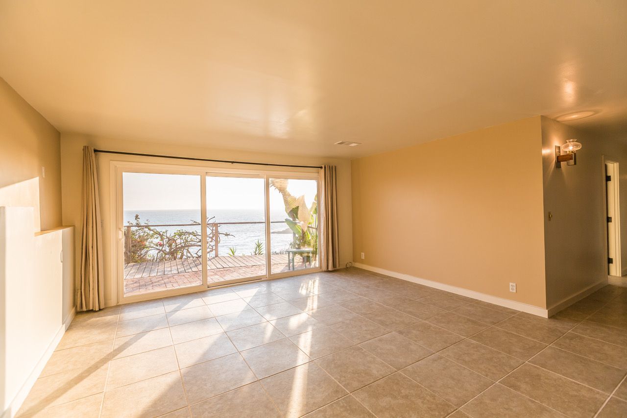Empty room with large sliding glass doors overlooking the ocean; tan walls and tiled floor.