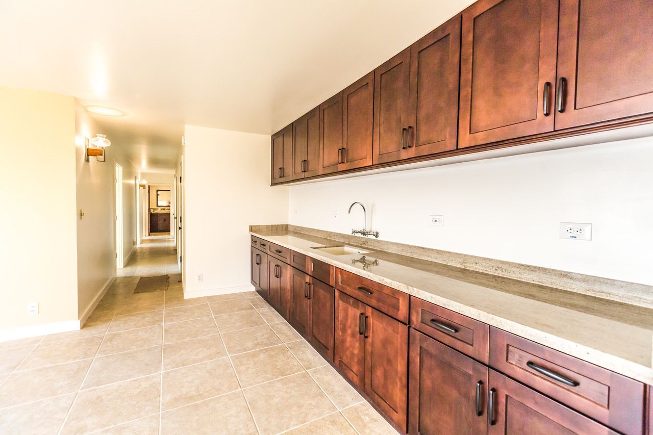 Long, narrow room with dark wood cabinets, light countertops, and a sink. The floor is tiled.