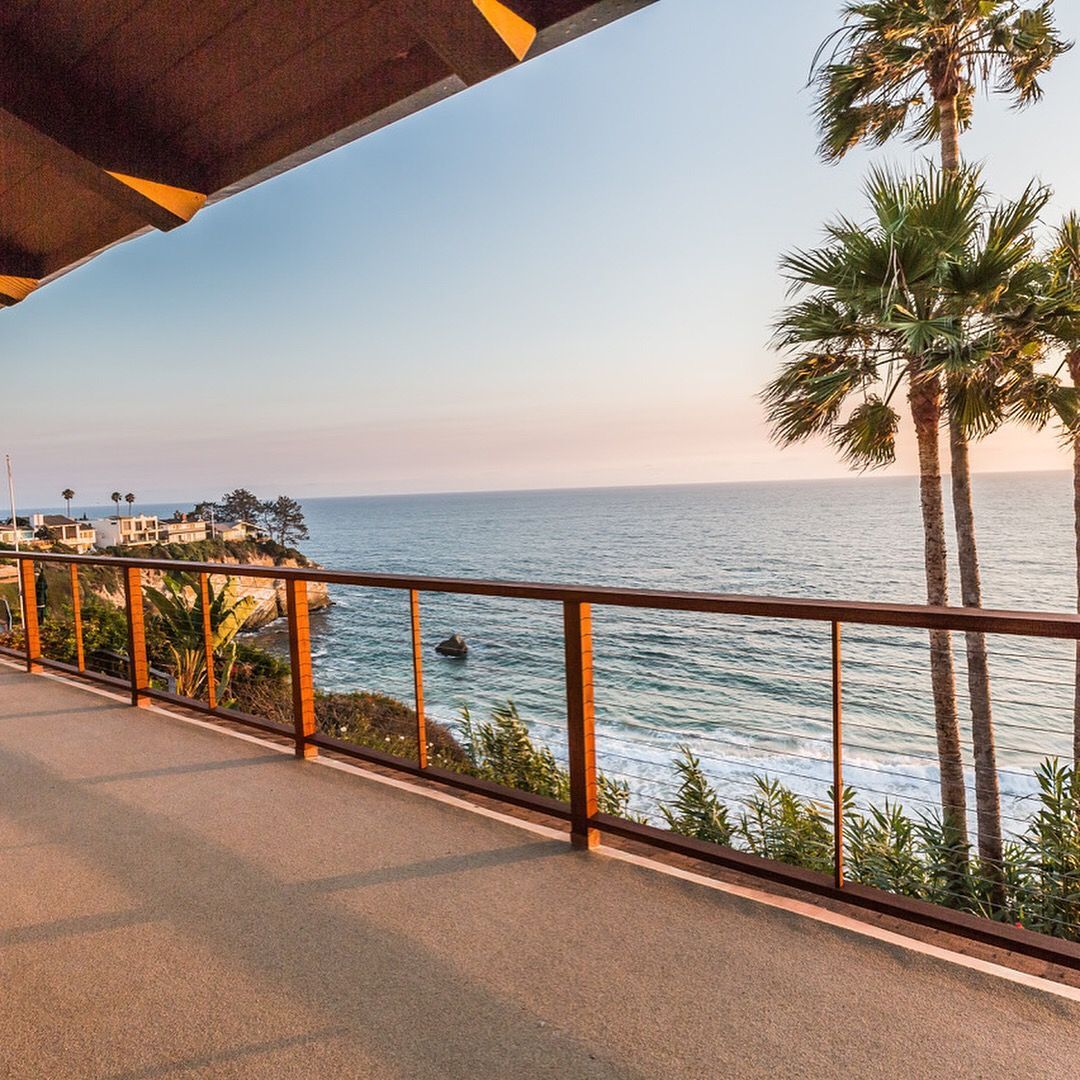 Ocean view from a balcony at sunset, palm trees, water, and coastline.