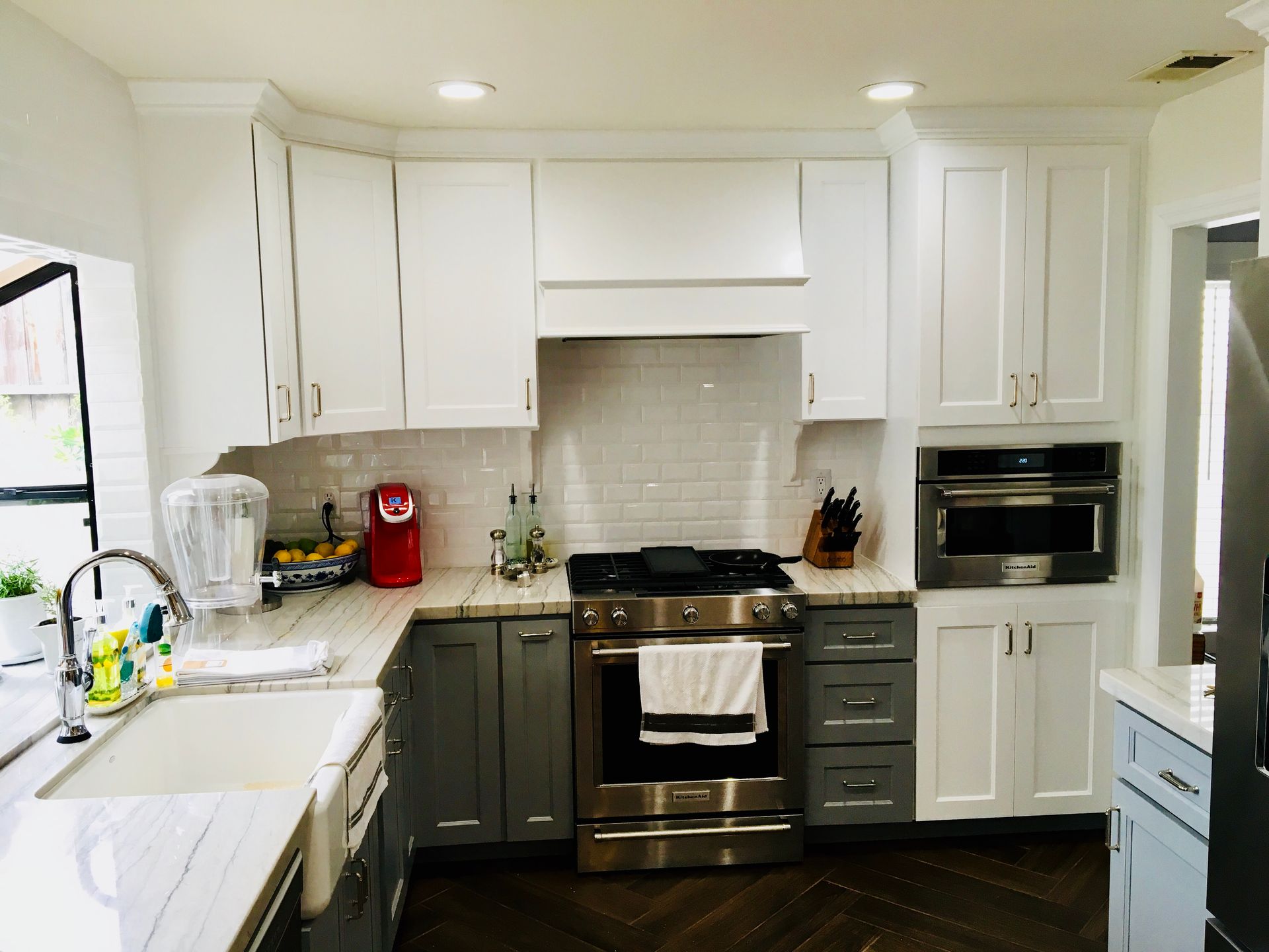 A bright kitchen with white upper cabinets, grey lower cabinets, and stainless steel appliances.