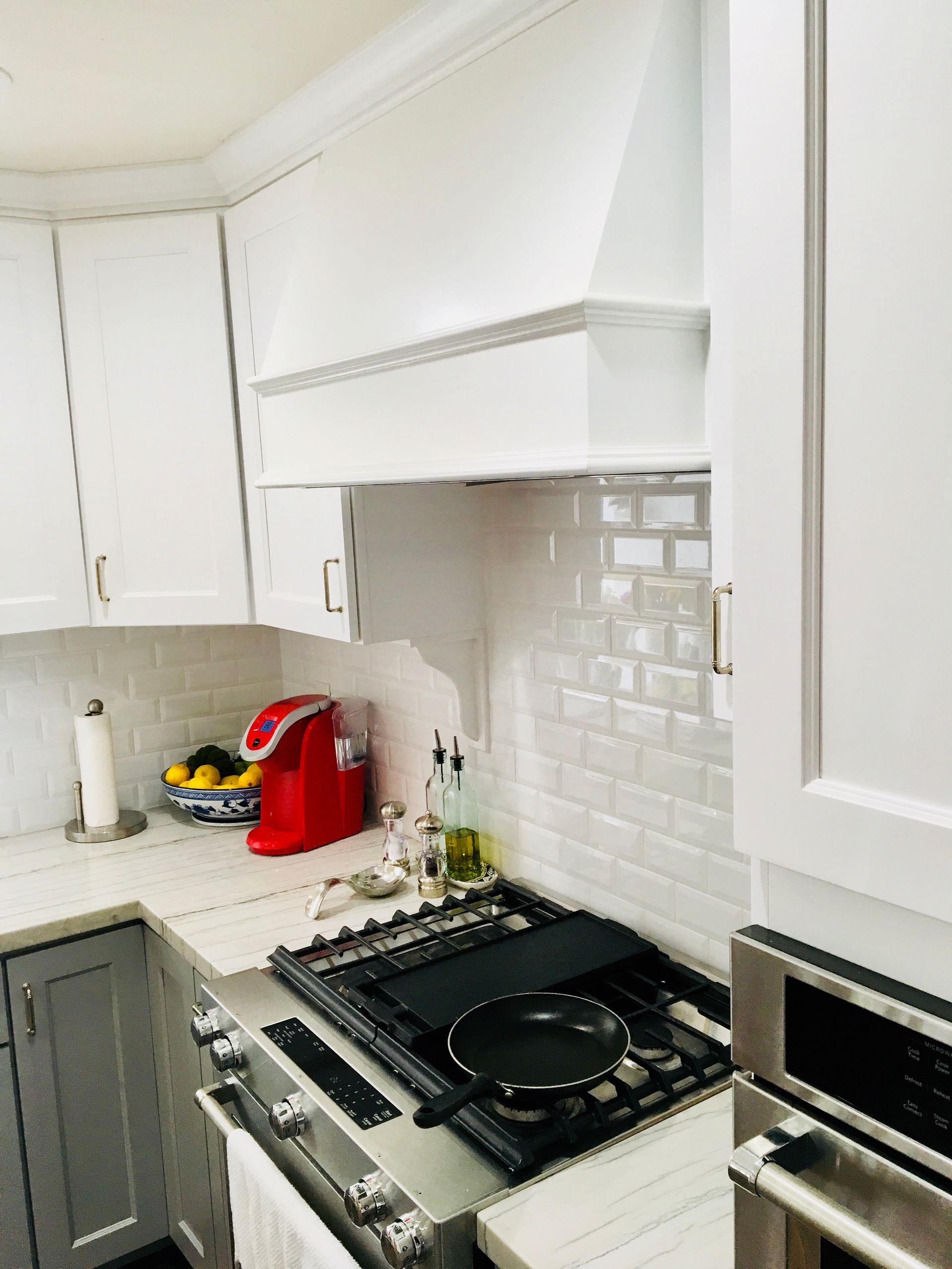 White kitchen with stove, range hood, and cabinets; a red coffee maker sits on the counter.