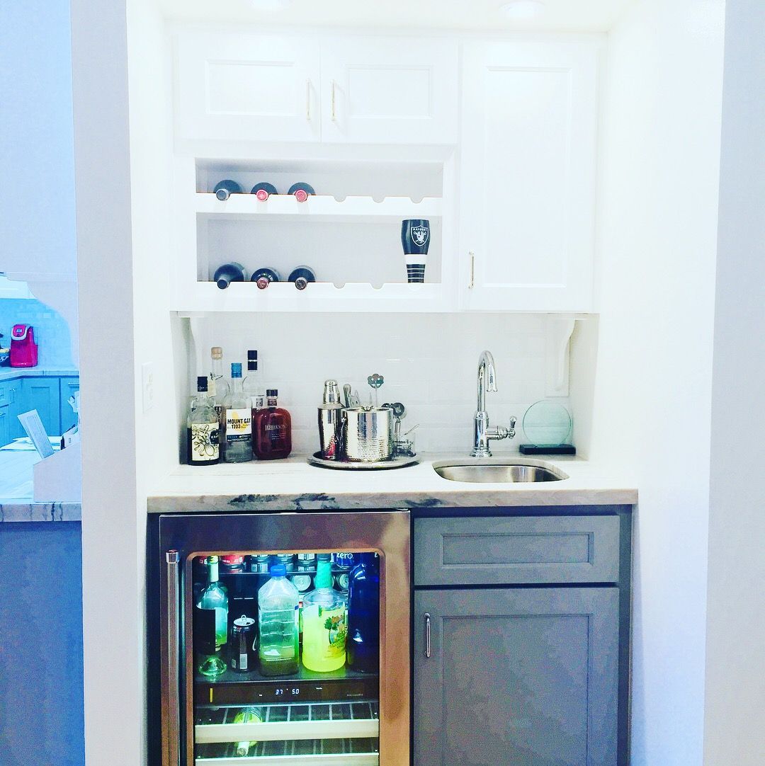 Small home bar nook with a wine fridge, sink, cabinets, and wine rack.