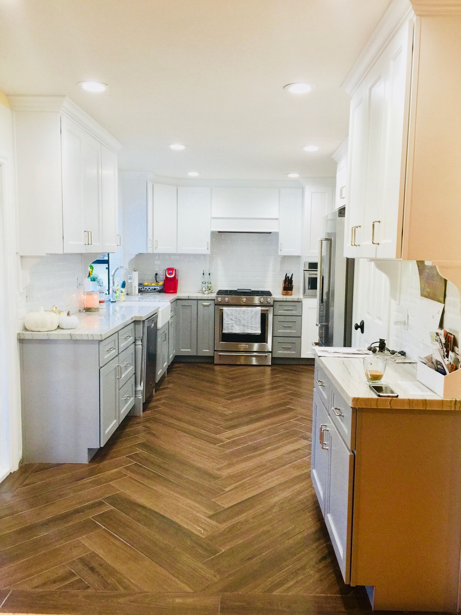Herringbone wood floor kitchen with white and gray cabinets, stainless steel appliances.