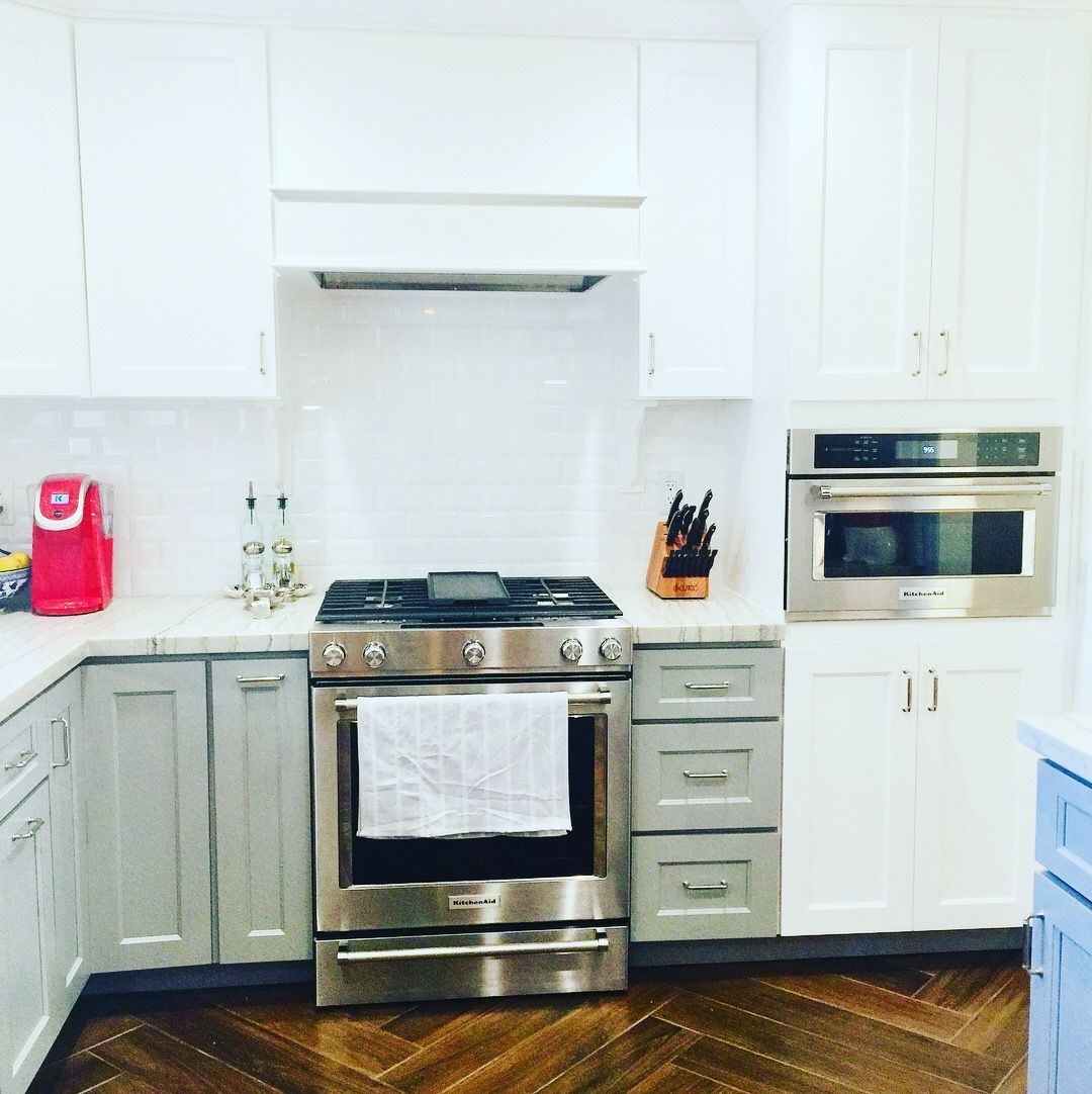 A kitchen with white and gray cabinets, stainless steel appliances, and a dark wood floor.