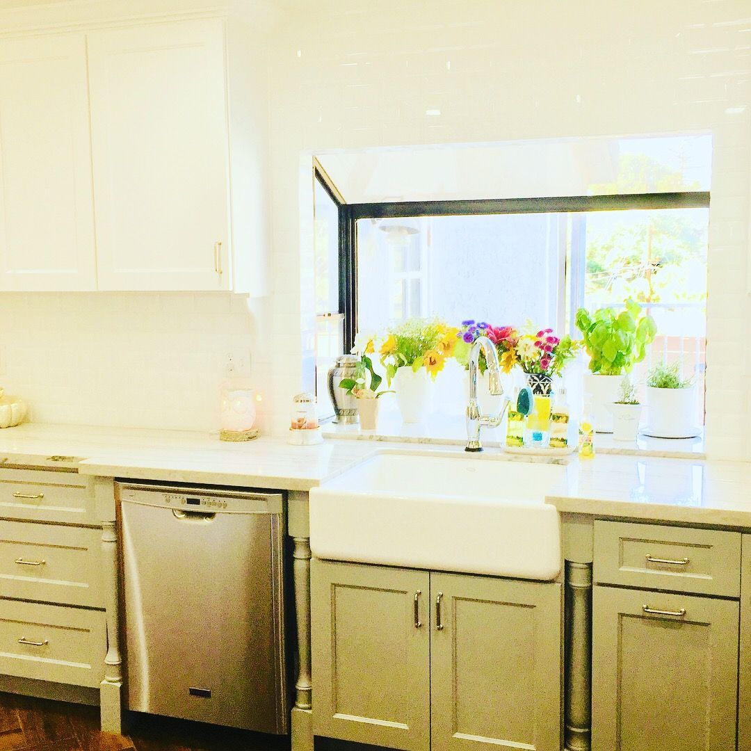 Kitchen with white cabinets, gray lower cabinets, stainless steel appliances, and a window with flowers.