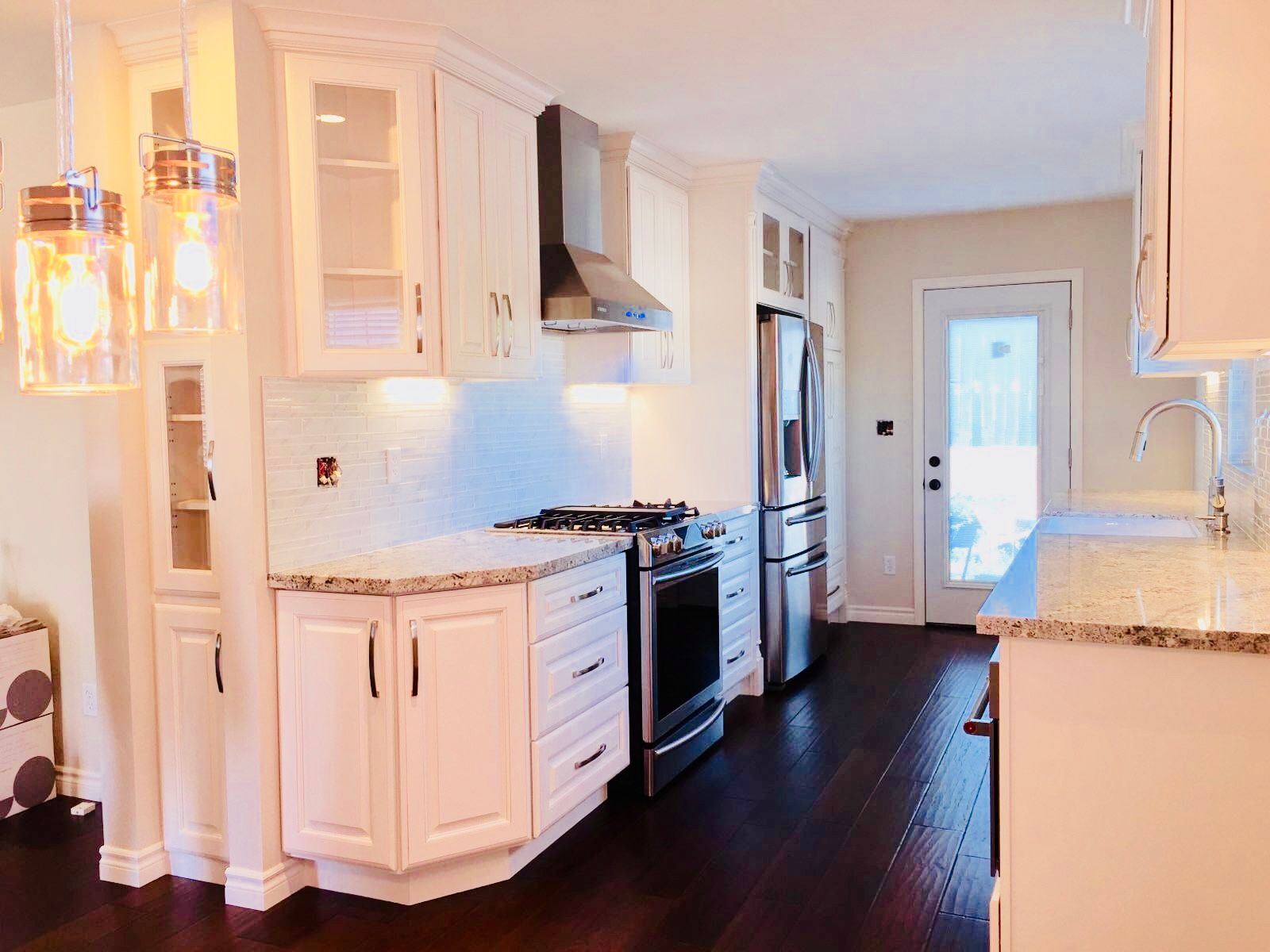 White kitchen with stainless steel appliances and dark wood floors.