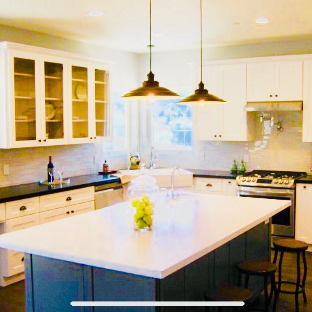 Kitchen with white cabinets, dark countertops, blue island, and pendant lights.