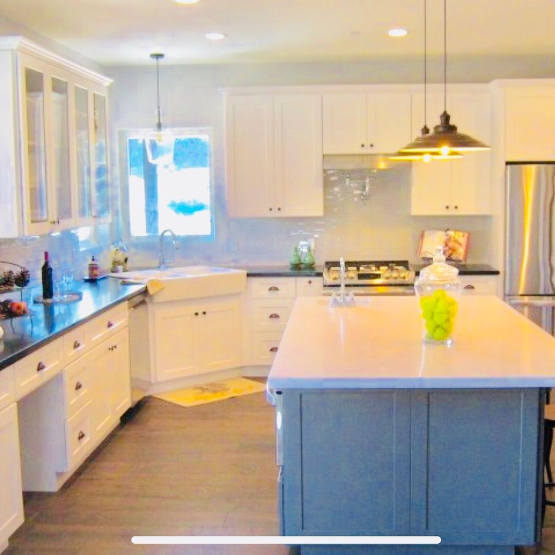 White kitchen with blue-gray island, black countertops, stainless steel appliances, and pendant lights.