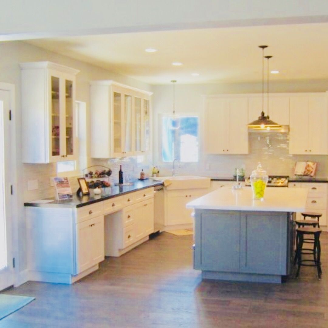 White kitchen with gray island, dark countertops, and wooden floor.