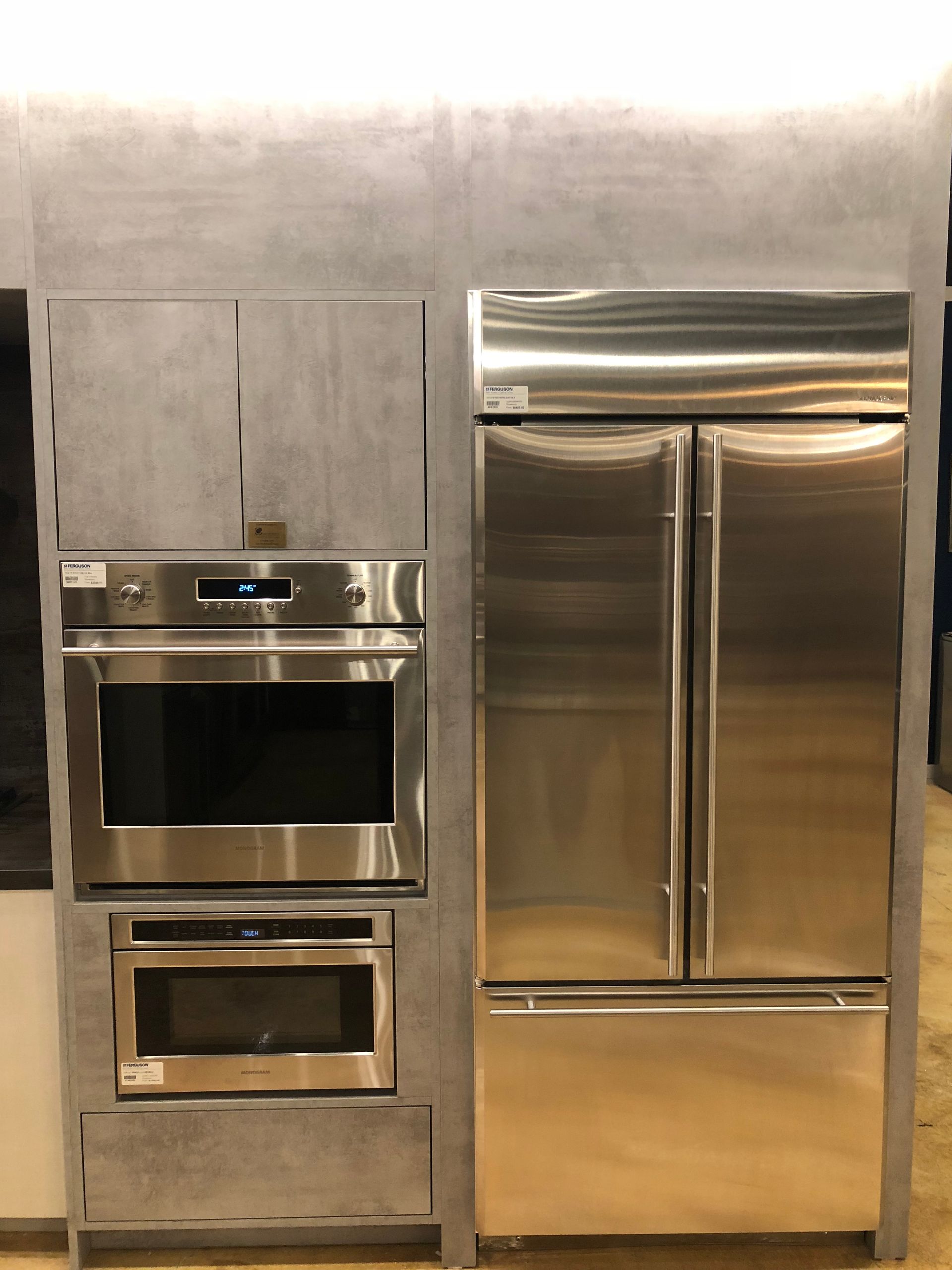 Stainless steel oven, microwave, and refrigerator built into a gray cabinet unit.