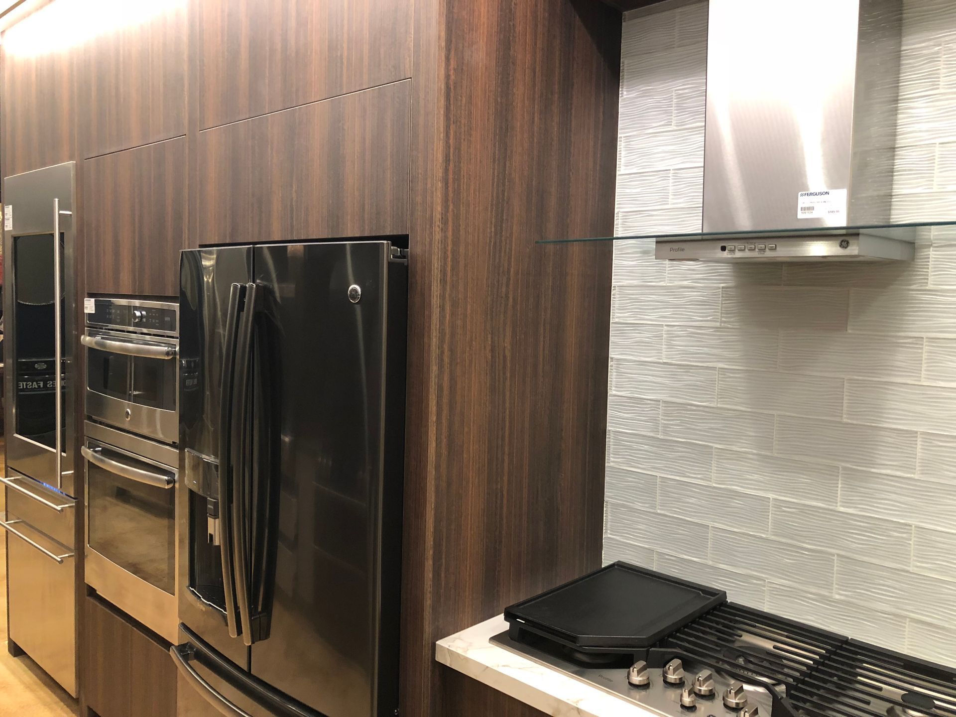 Stainless steel kitchen appliances against wood paneling and a tiled backsplash.