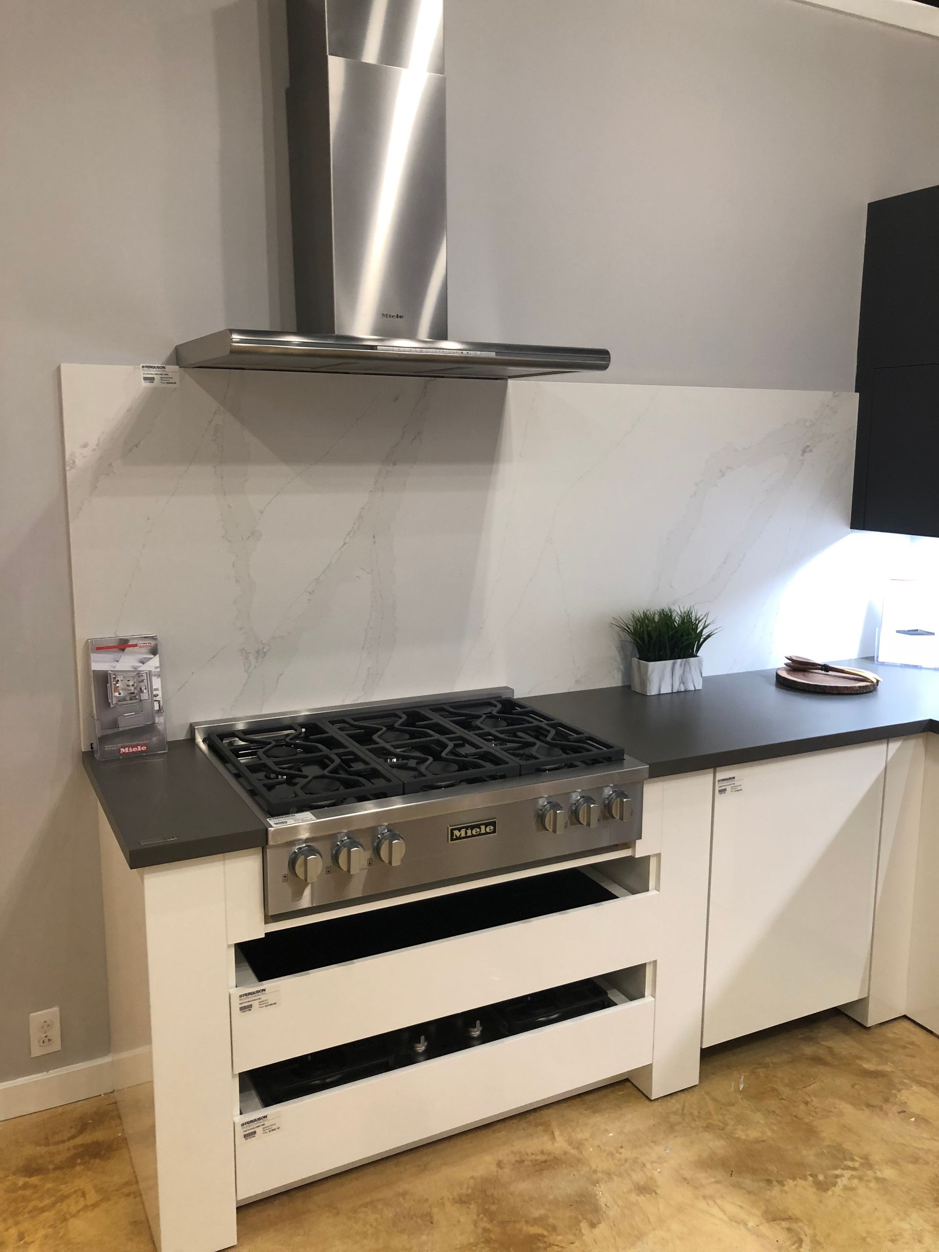 Stainless steel range with hood in a kitchen; white cabinetry, dark countertop.