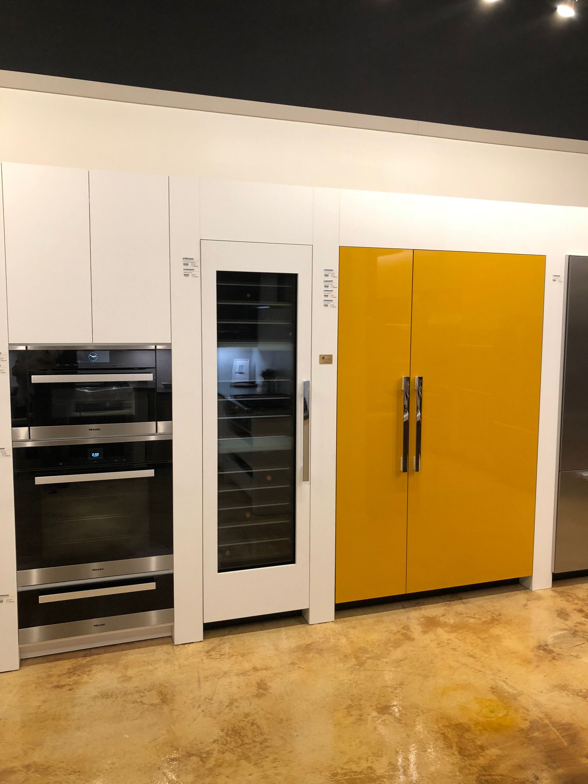 A modern kitchen with a yellow refrigerator, white cabinets, oven, and wine cooler.