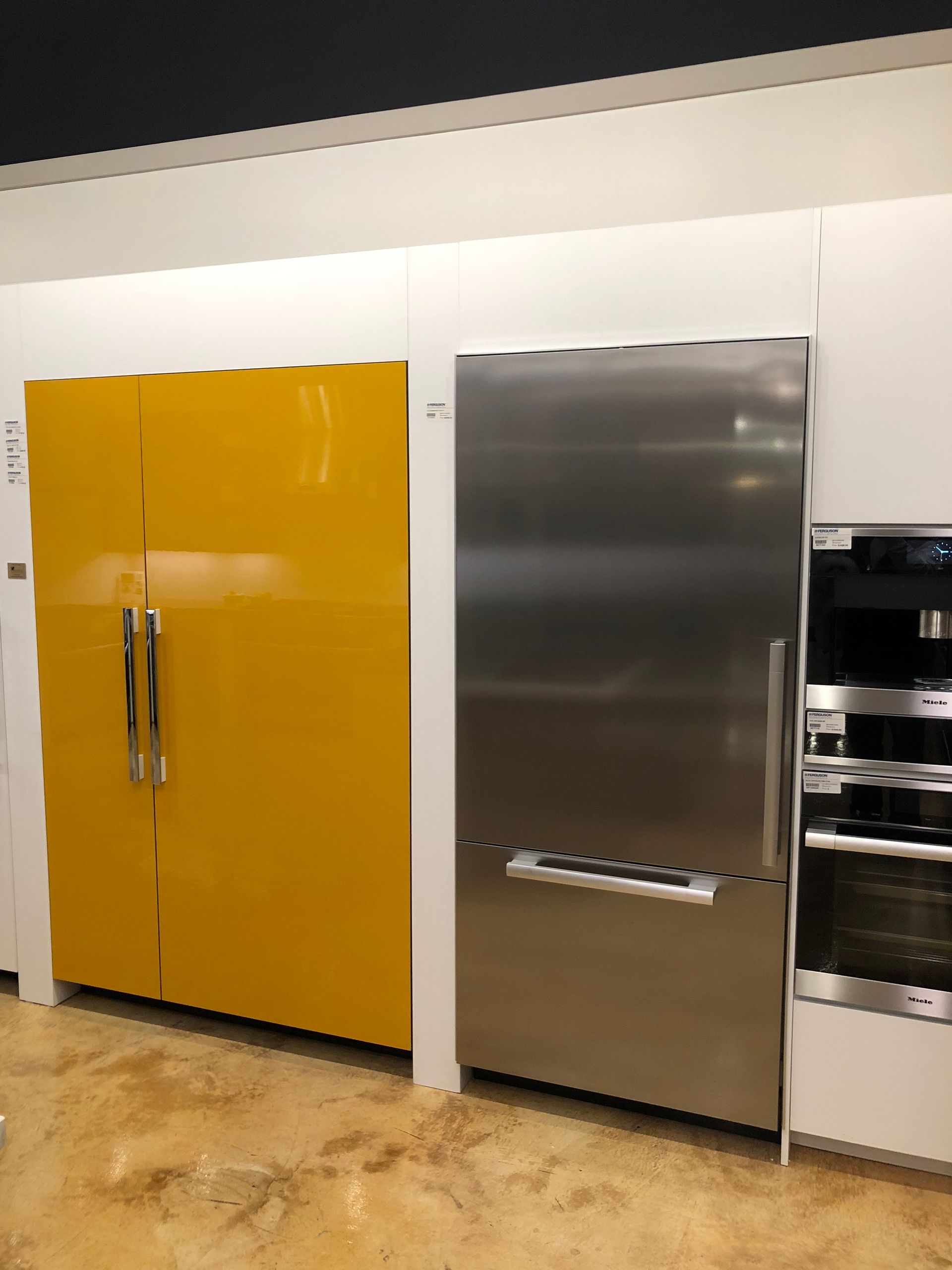Yellow and stainless steel refrigerators side-by-side in a showroom setting.