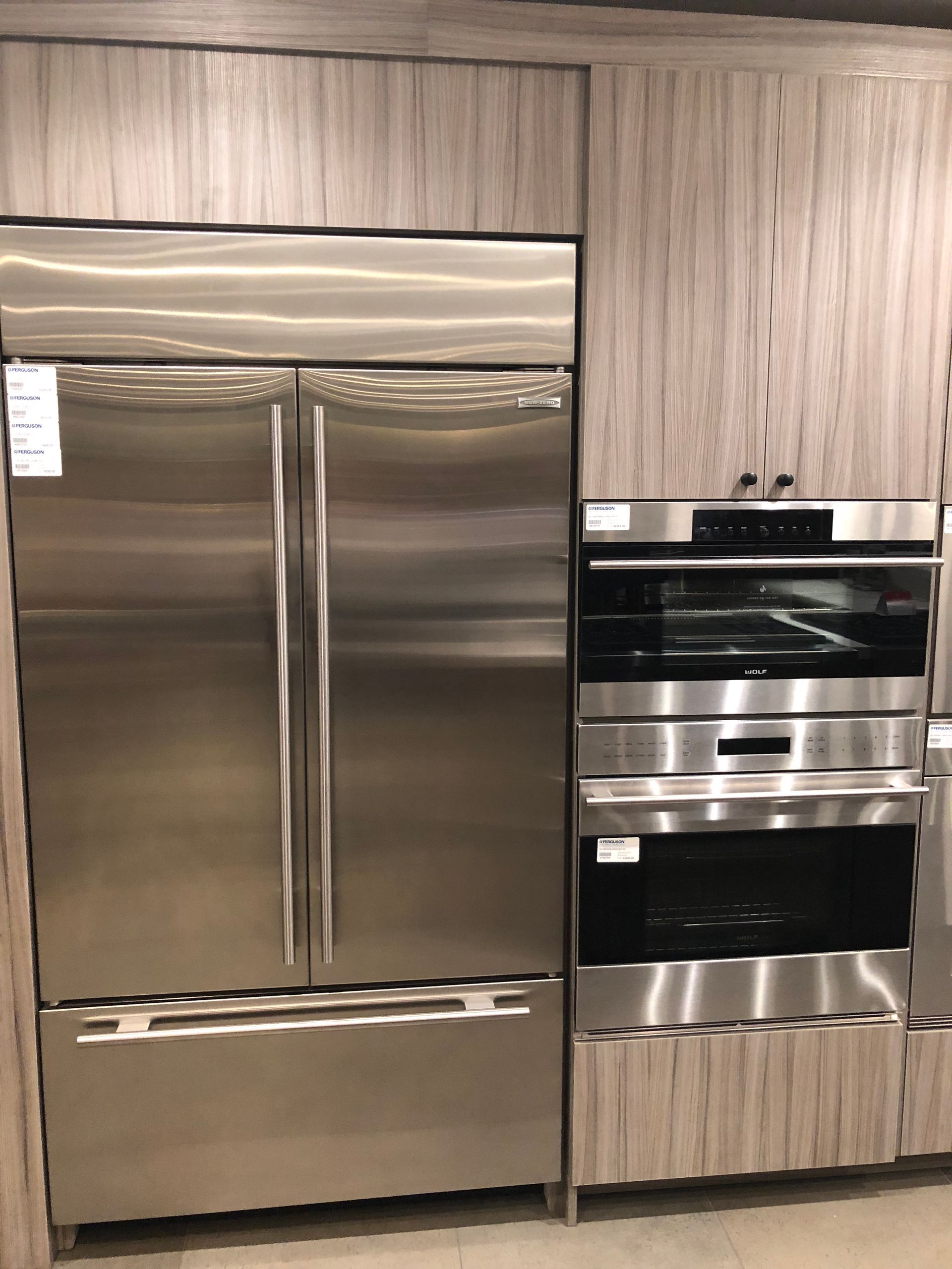 Stainless steel refrigerator and ovens built into light wood cabinets.