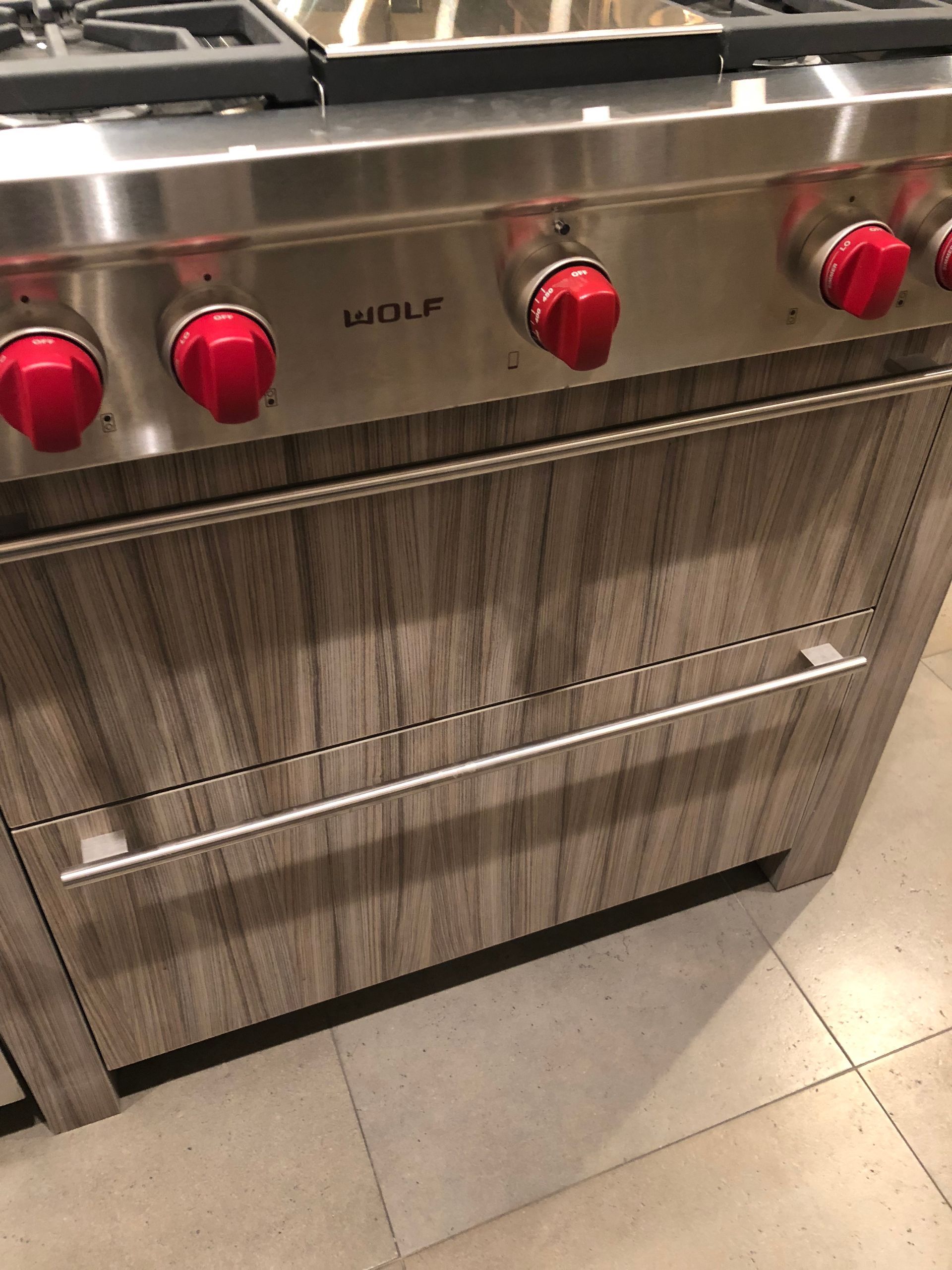 Wolf range with red knobs and a wooden grain drawer.