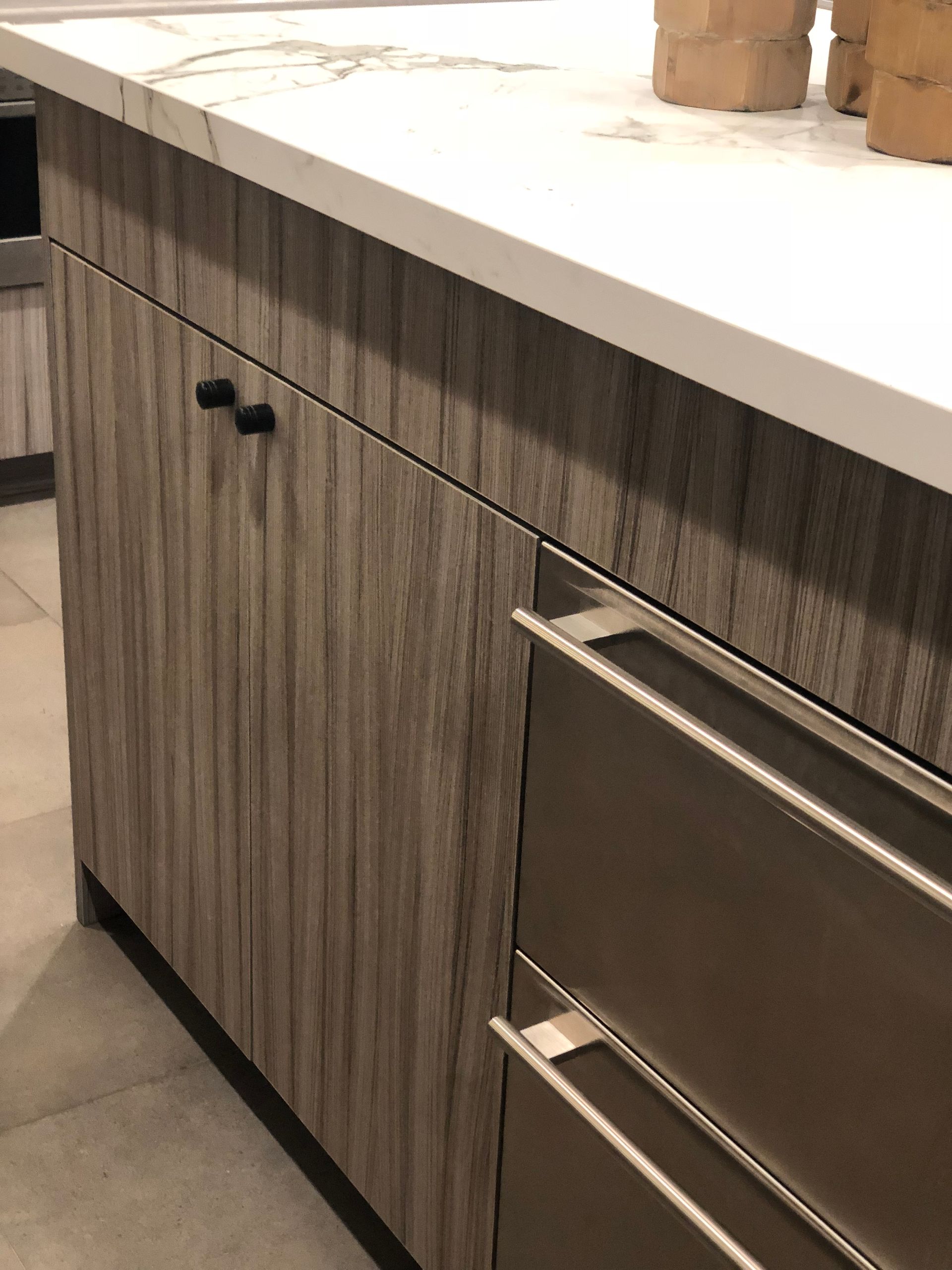 Kitchen cabinetry with wood grain finish, black hardware, and stainless steel drawers below a countertop.