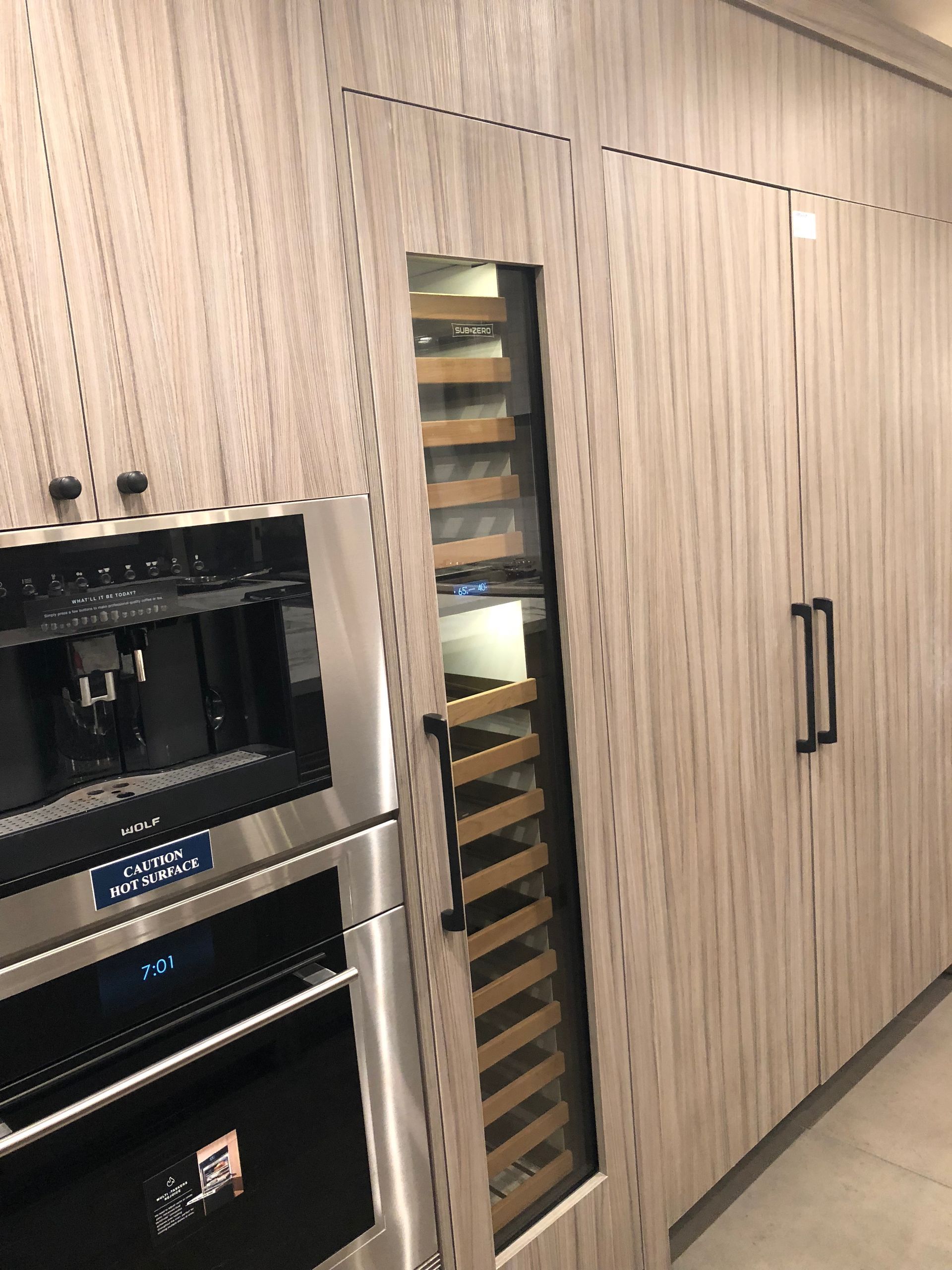 A built-in kitchen area with stainless steel appliances, a wine cooler, and light wood cabinets.