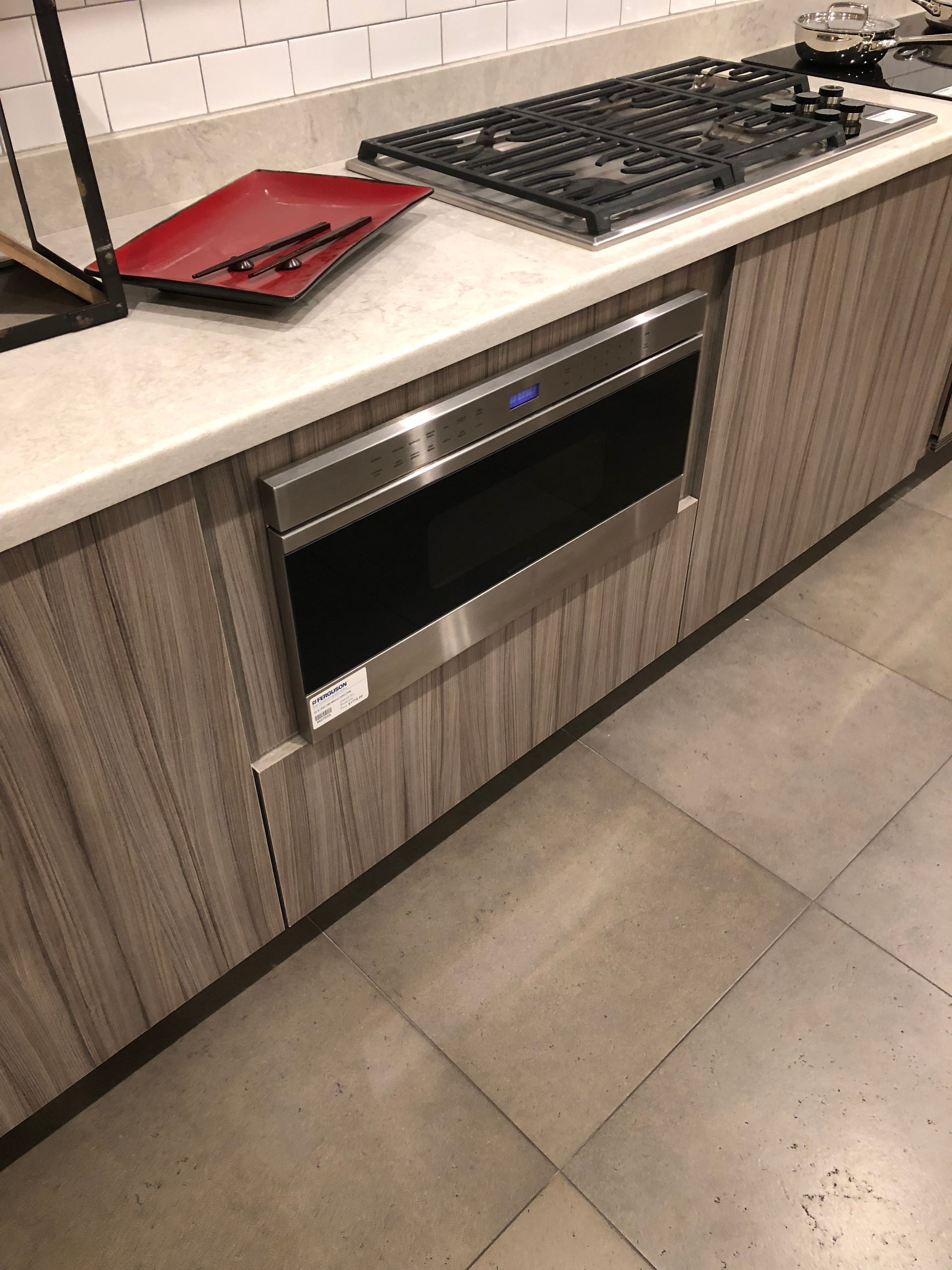 Built-in stainless steel microwave oven under a countertop next to a gas cooktop in a kitchen.