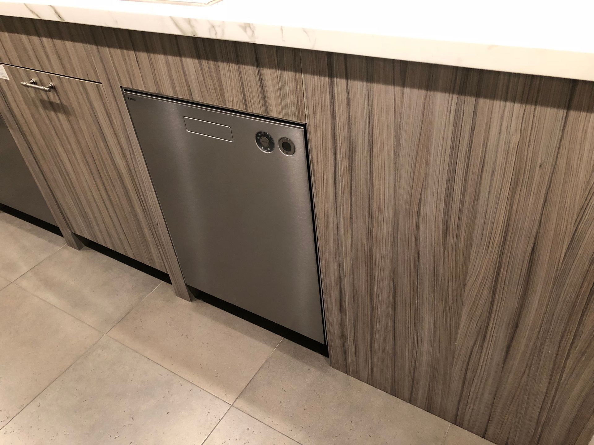 Stainless steel dishwasher in a kitchen with light wood cabinets.