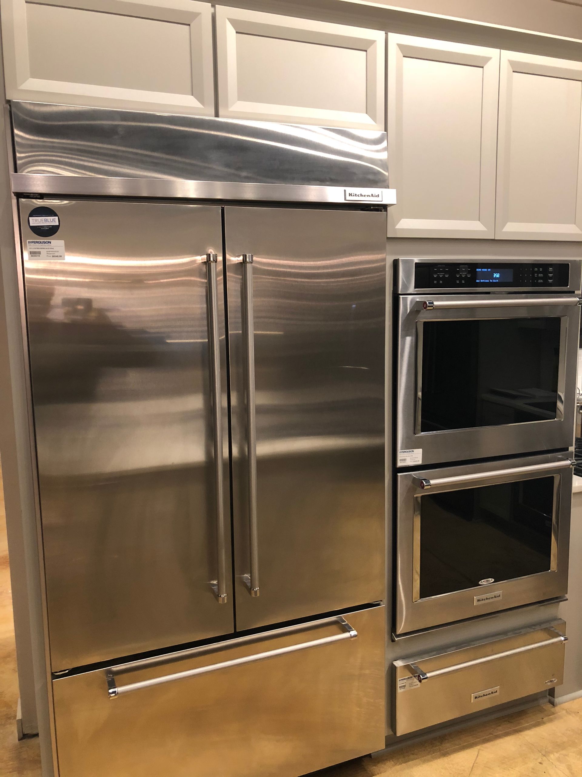 Stainless steel refrigerator and double ovens built into light gray cabinets.