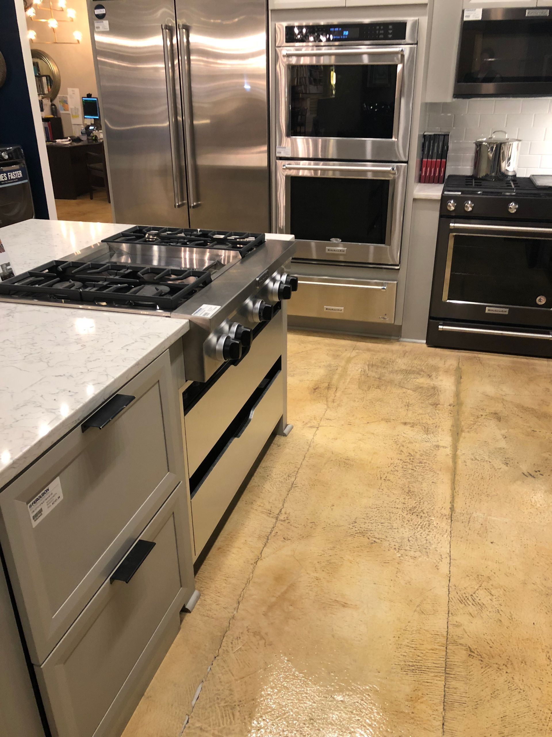 A kitchen with stainless steel appliances, including a gas cooktop on a light gray island, a double oven, and a refrigerator.