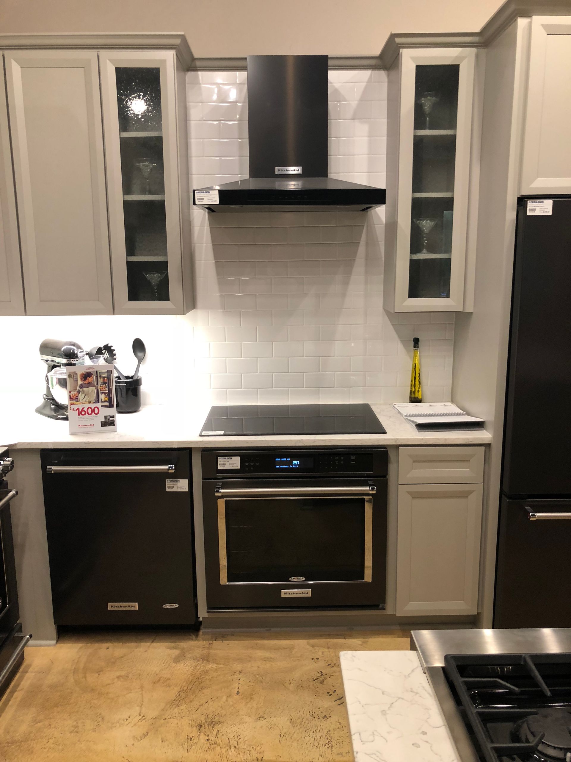 Modern kitchen with grey cabinets, black appliances, white subway tile backsplash, and stainless range hood.