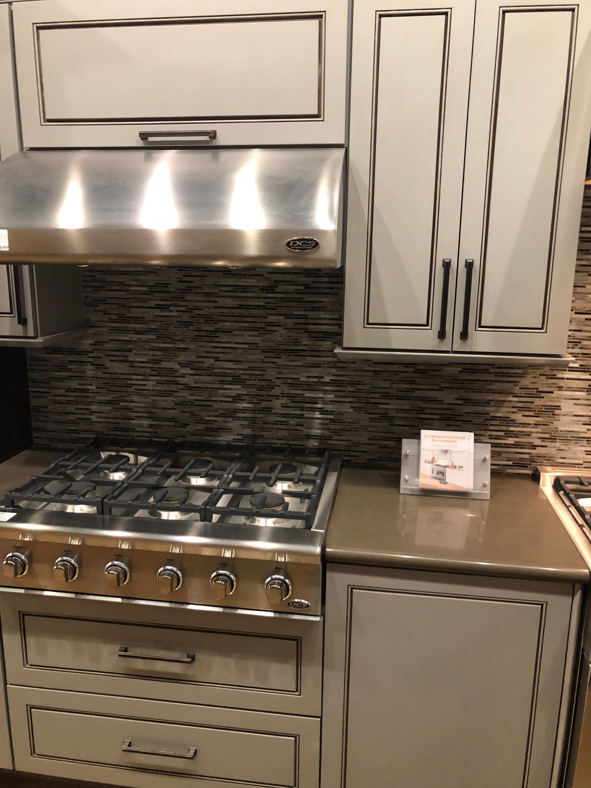 Kitchen with light gray cabinets, stainless steel stove, brown backsplash, and range hood.