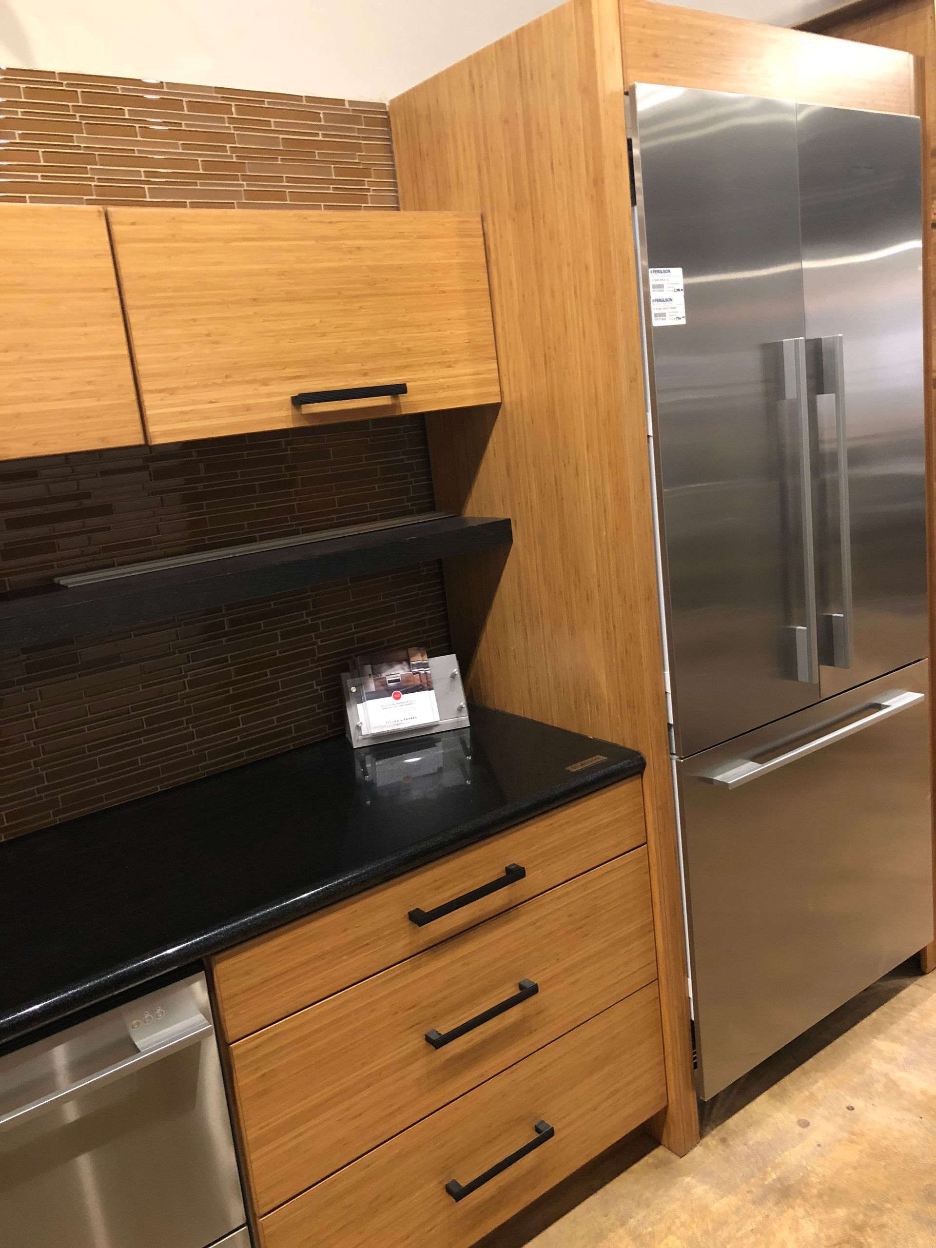 Kitchen with bamboo cabinets, stainless steel appliances, and black countertops.