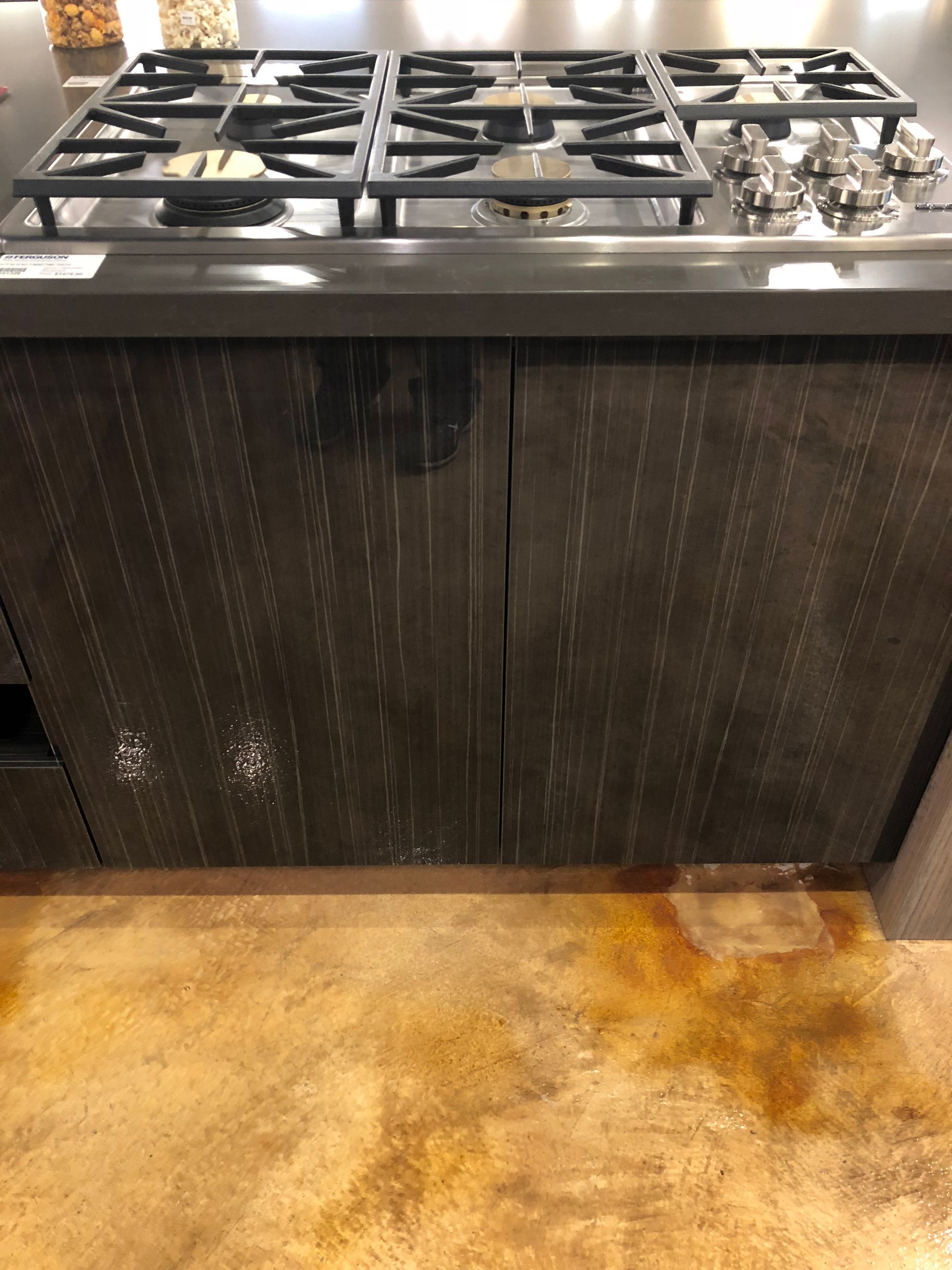 Stovetop with dark wood cabinets, mounted on a brown, speckled concrete floor.