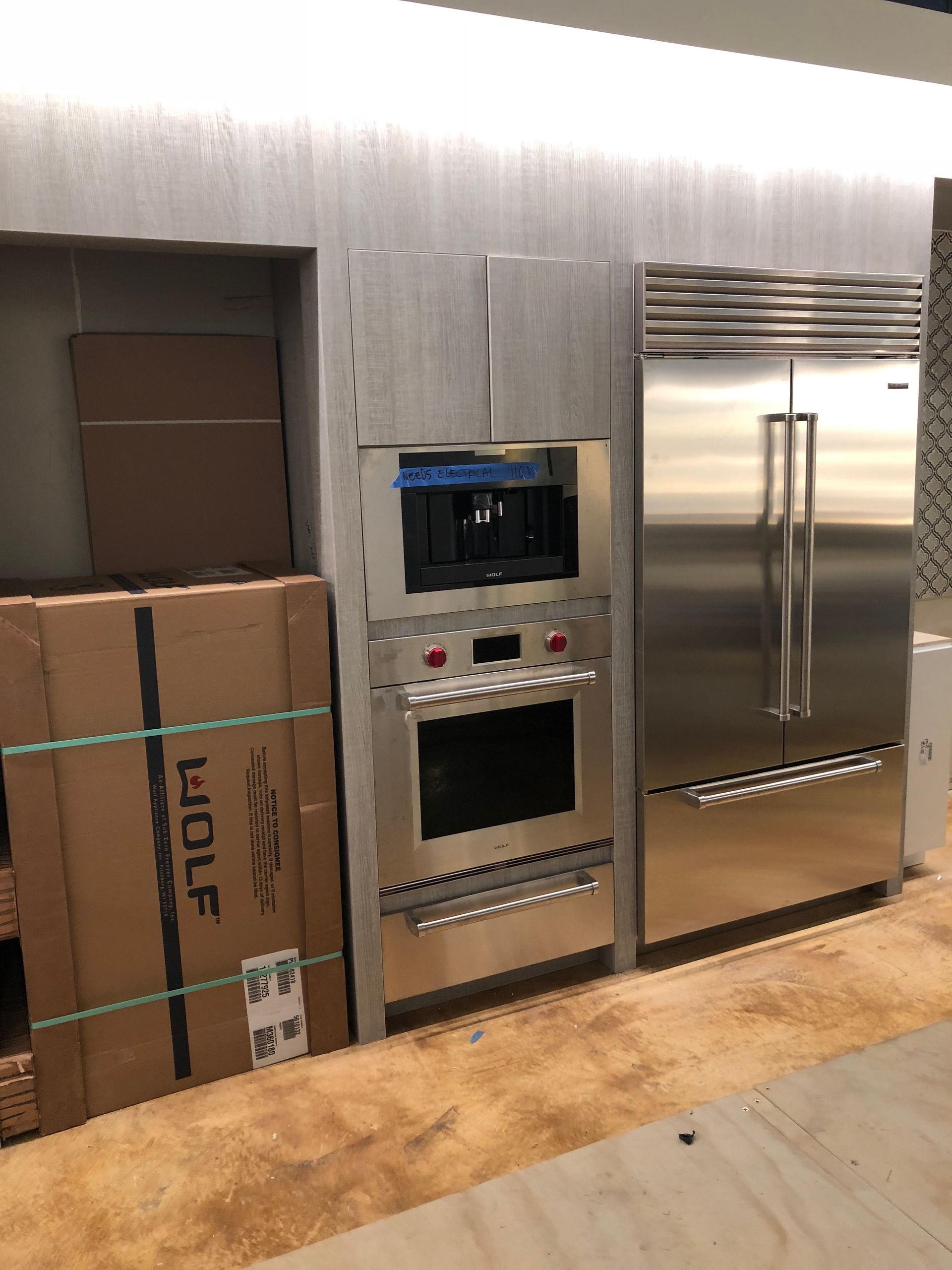 Stainless steel kitchen appliances: oven, coffee maker, refrigerator. Cardboard boxes on the left.