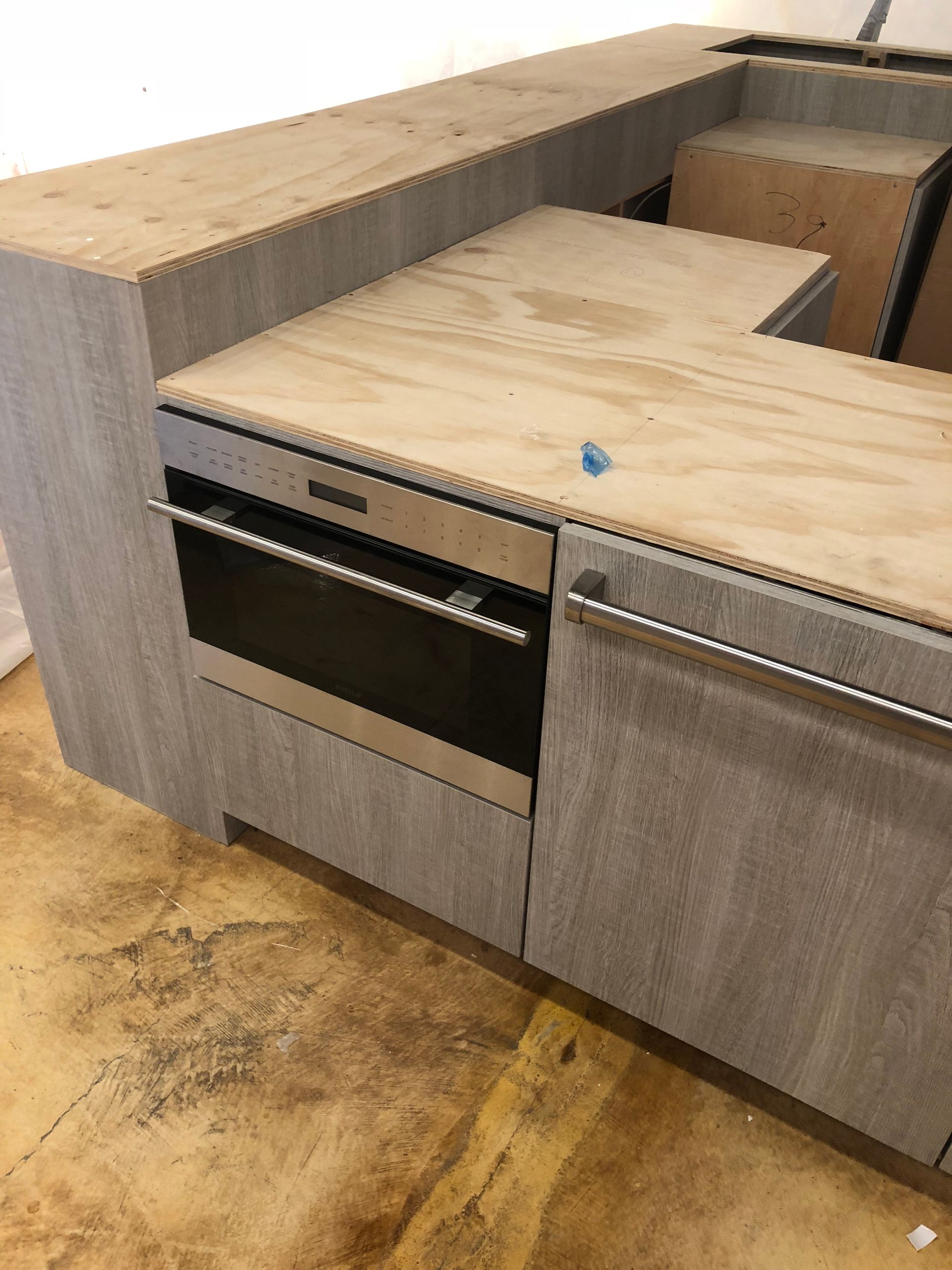 Kitchen cabinets with an oven installed, countertop, unfinished plywood, and wood grain finish.