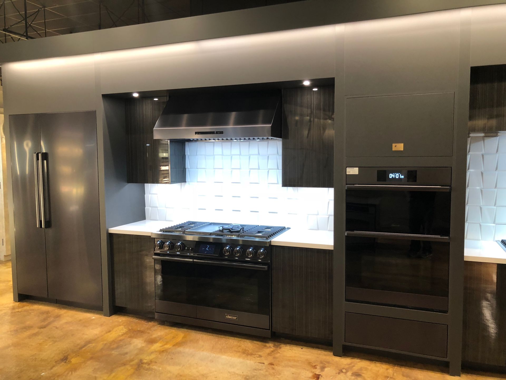 Modern kitchen with dark gray cabinetry, stainless steel appliances, and white tile backsplash.